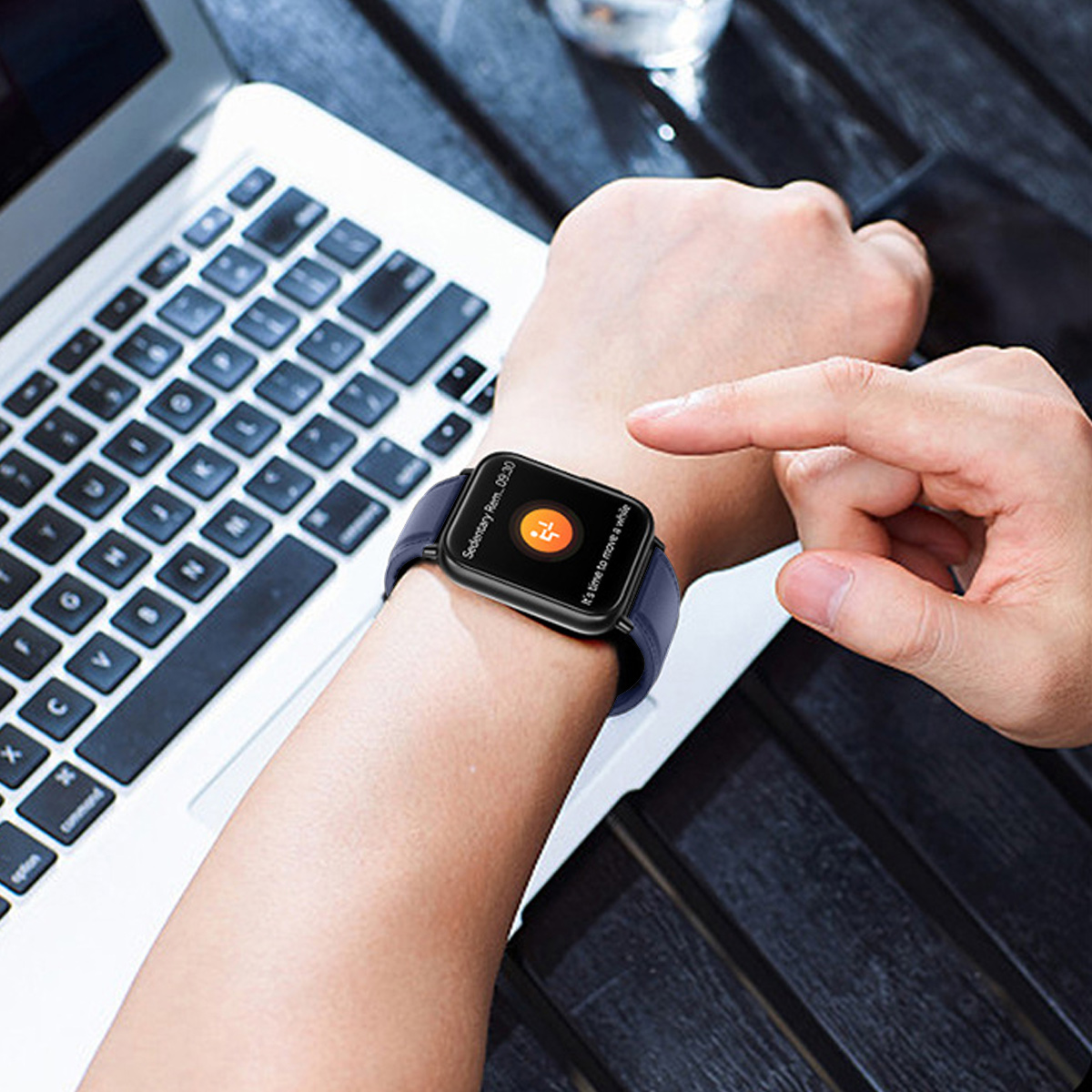 Hand mit Smartwatch, die Zeit anzeigt. Laptop im Hintergrund geöffnet.