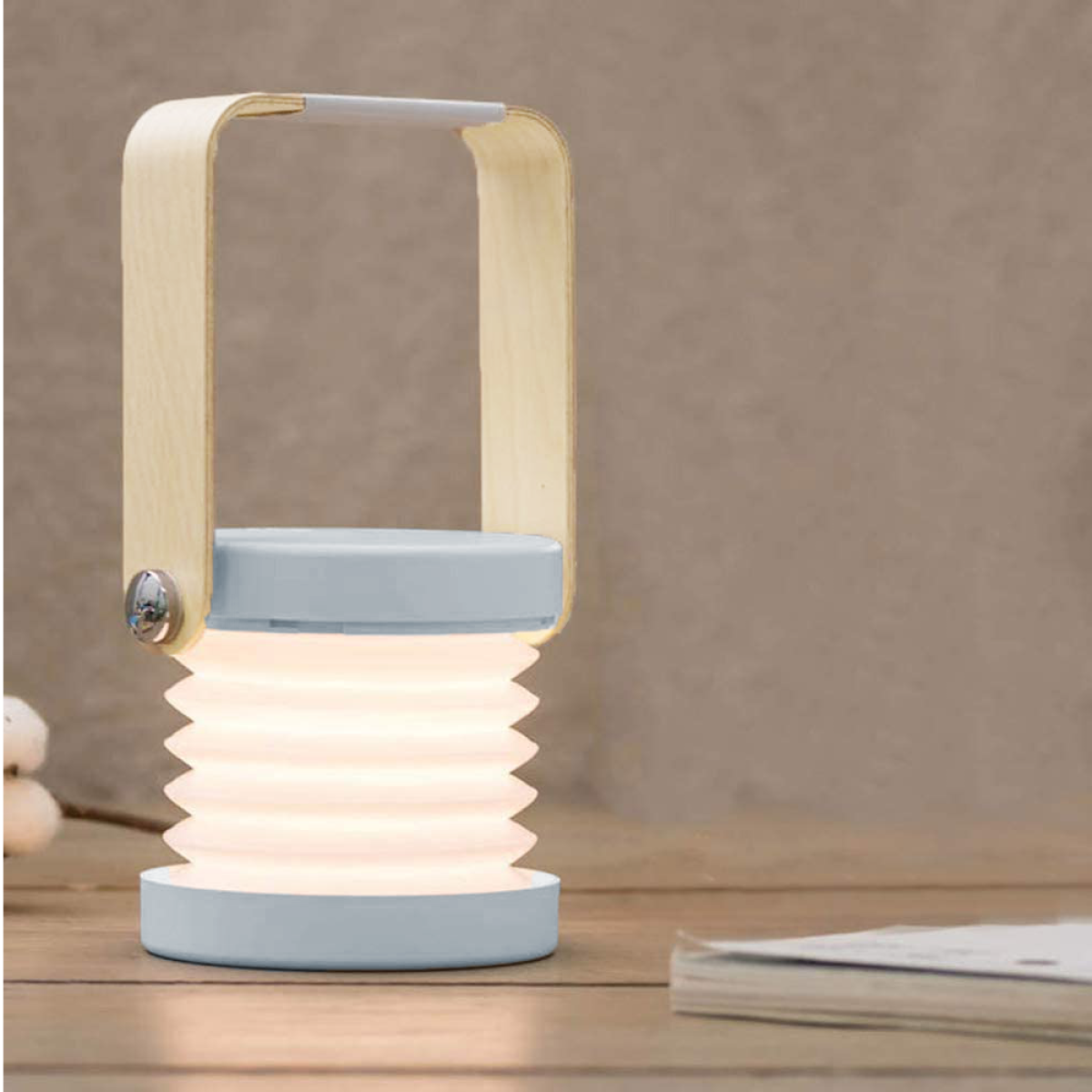 Lampe mit Holzgriff auf einem Holztisch, mit Licht und einem Stapel Bücher daneben.