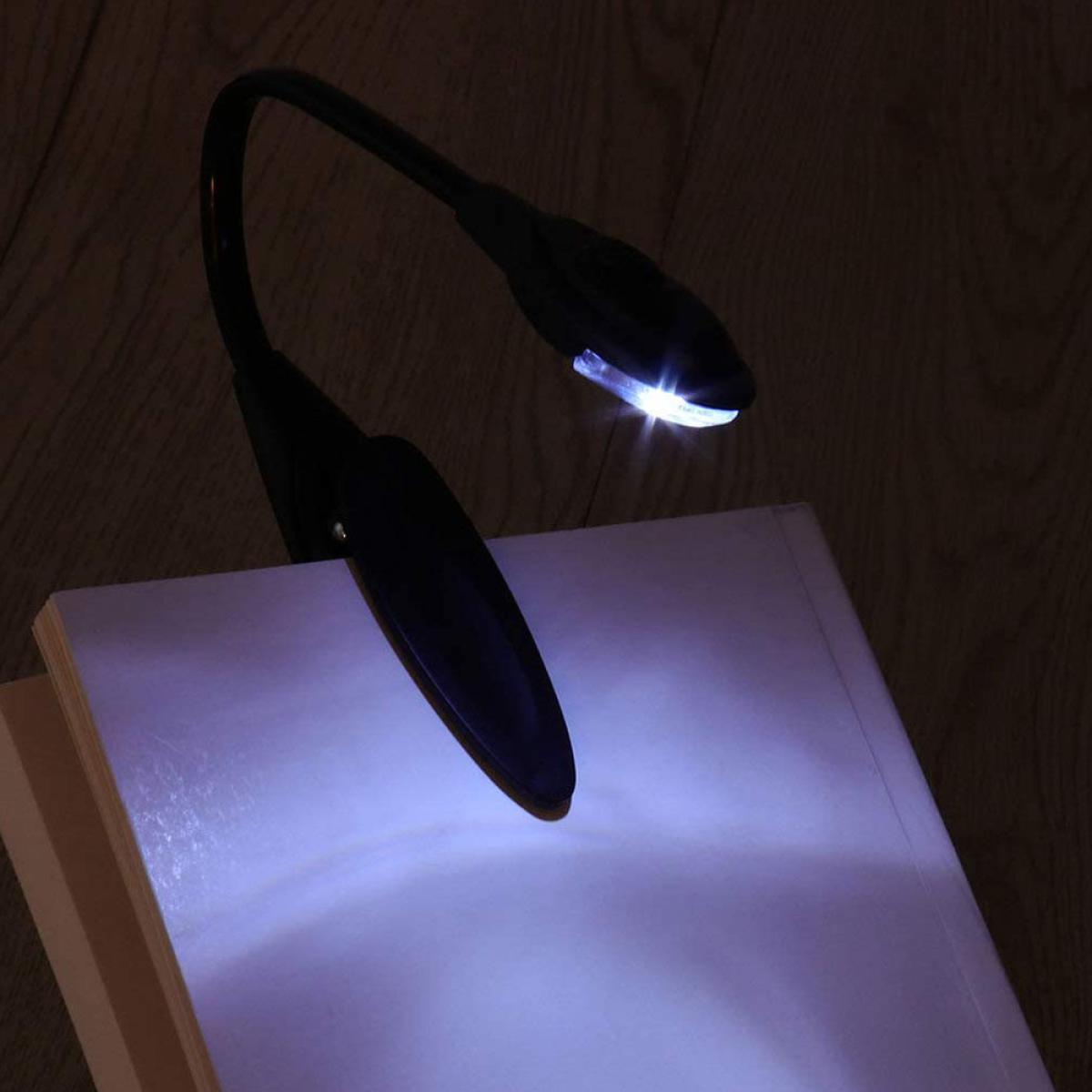 Schwarze Leselampe an einem Buch befestigt. Das Licht scheint auf die offenen Seiten und beleuchtet den Text.