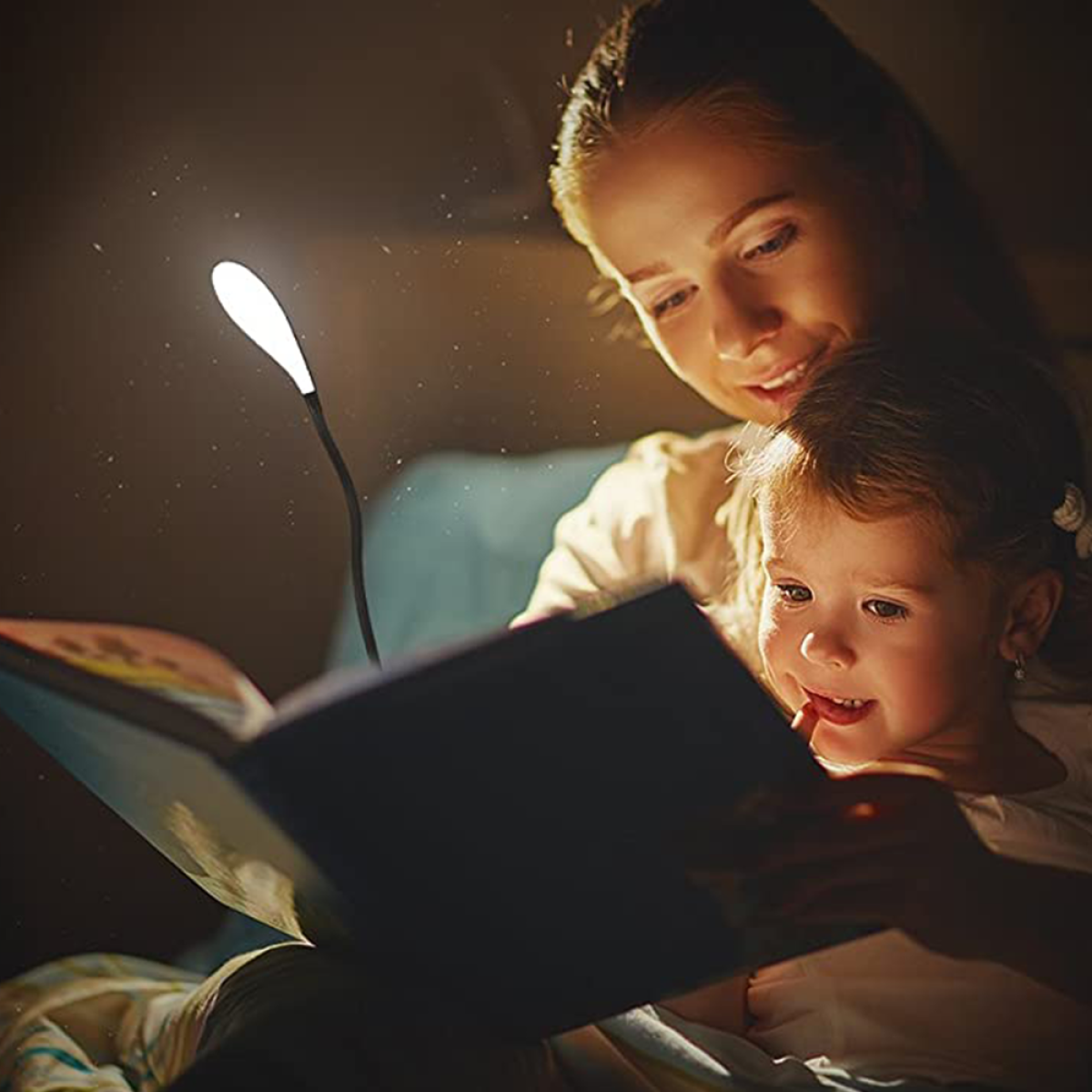 Mutter und Kind lesen Buch unter flexibler schwarzer Lampe in dunklem Raum.