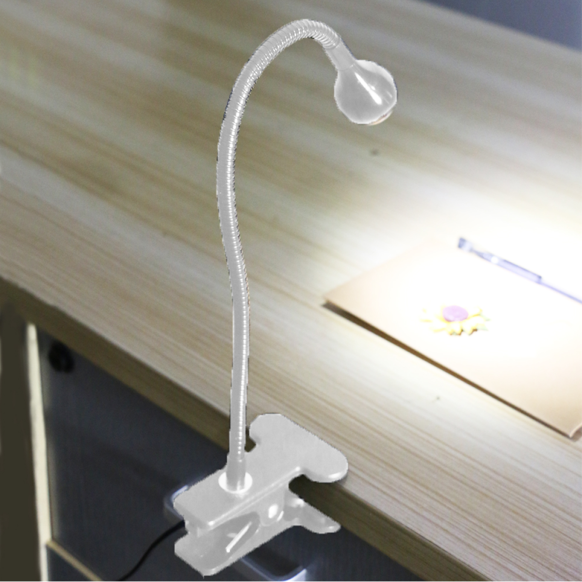Flexible Schreibtischlampe mit Clip-Sockel. Ein Stift und Blumen auf dem Tisch. Holzoberfläche.