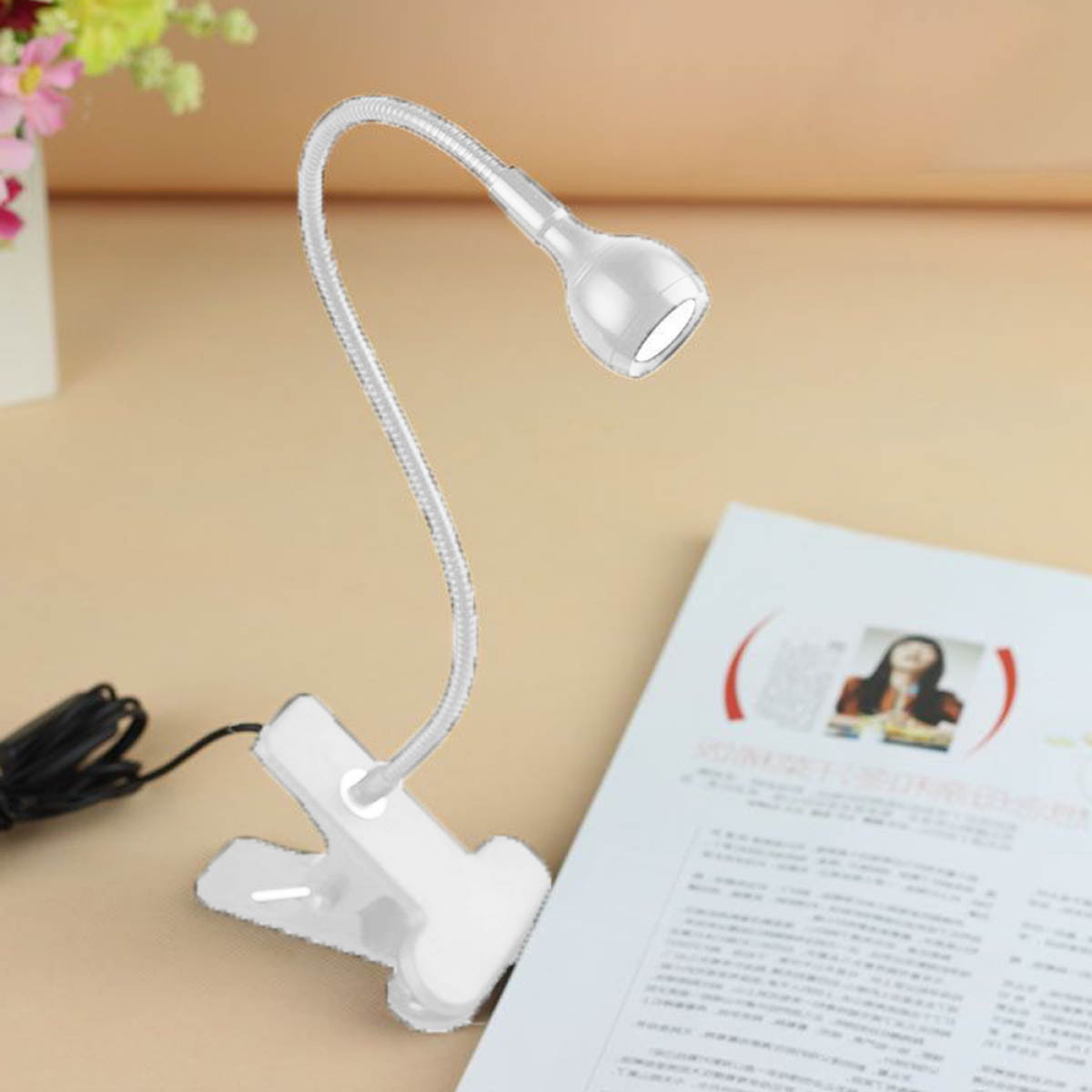 Kleine, weiße Clip-Schreibtischlampe mit flexiblem Arm, die ein Buch auf einem Tisch beleuchtet.