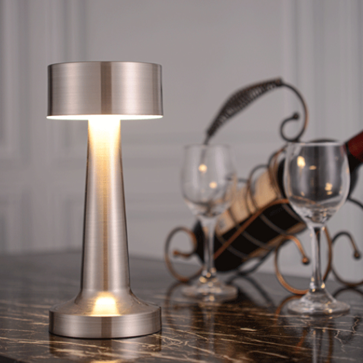 Eine silberne Lampe mit Licht, neben Weingläsern und einem Weinhalter.