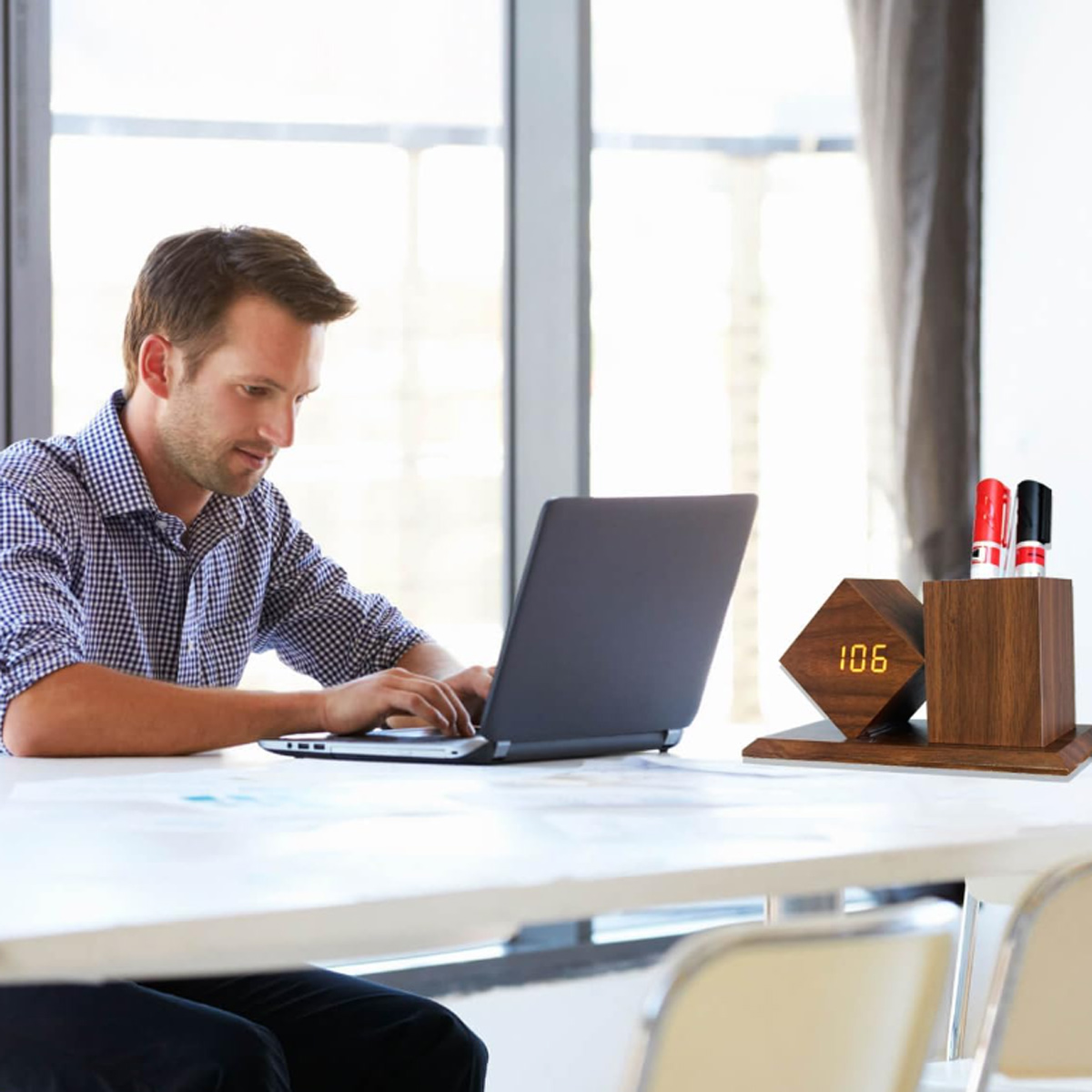 Mann arbeitet am Laptop am Schreibtisch, mit hölzerner Uhr und Stifthalter in der Nähe.