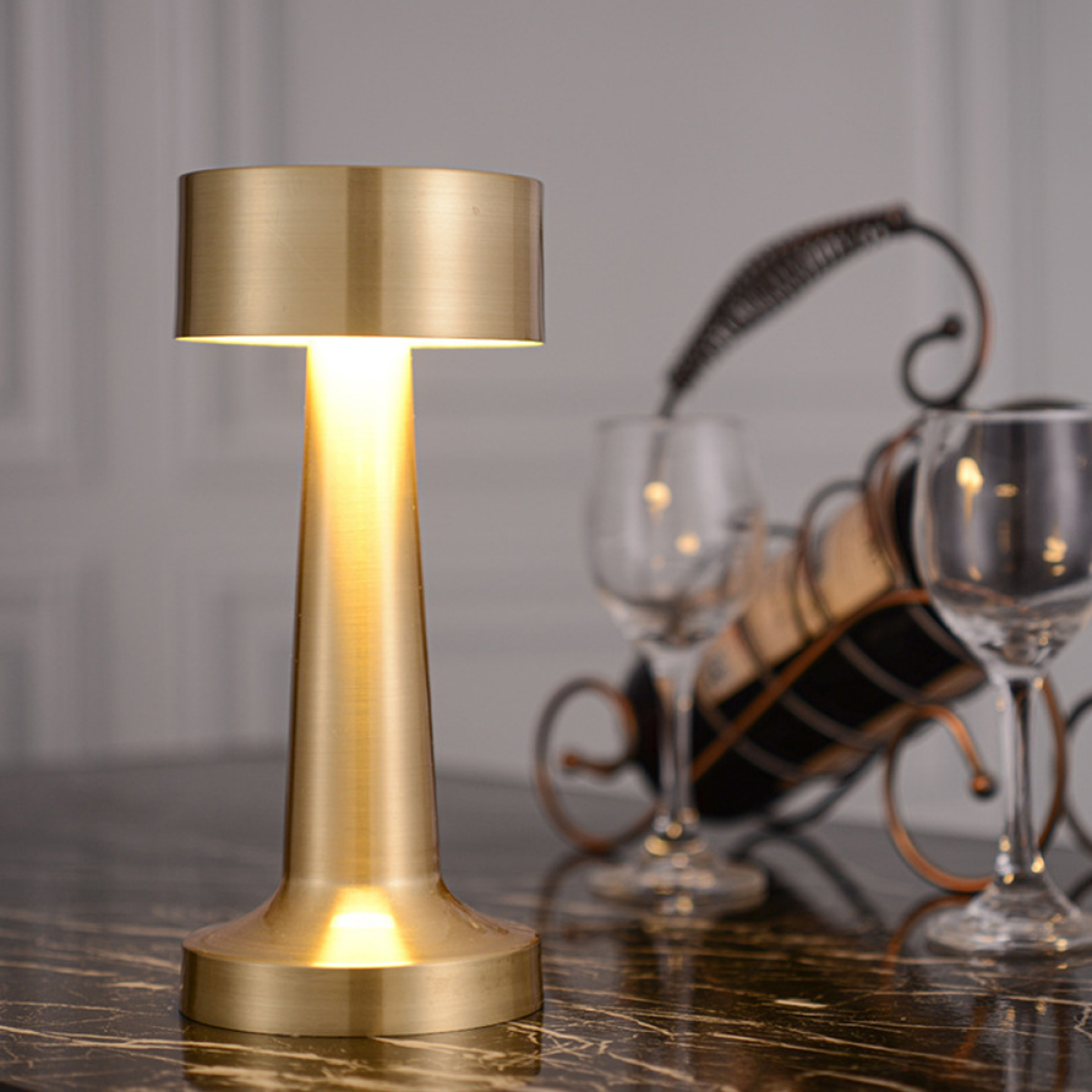 Eine goldfarbene Tischlampe mit hohem Fuß und nach oben strahlendem Licht.