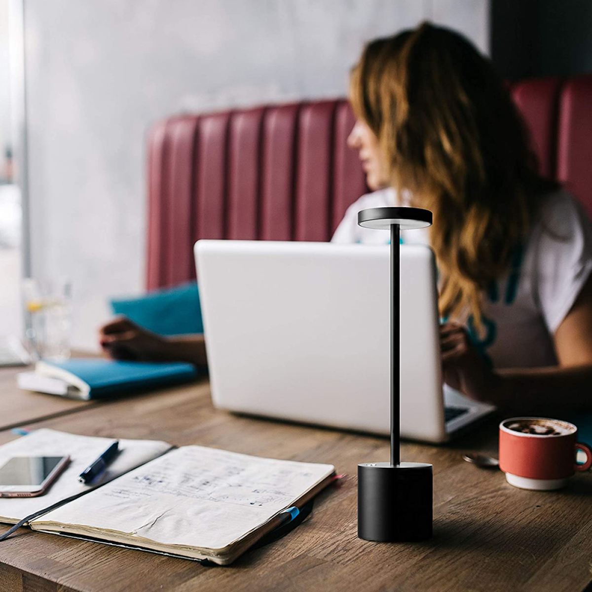 Schwarze Lampe auf einem Schreibtisch mit Laptop, Telefon und Notizbuch im Café.