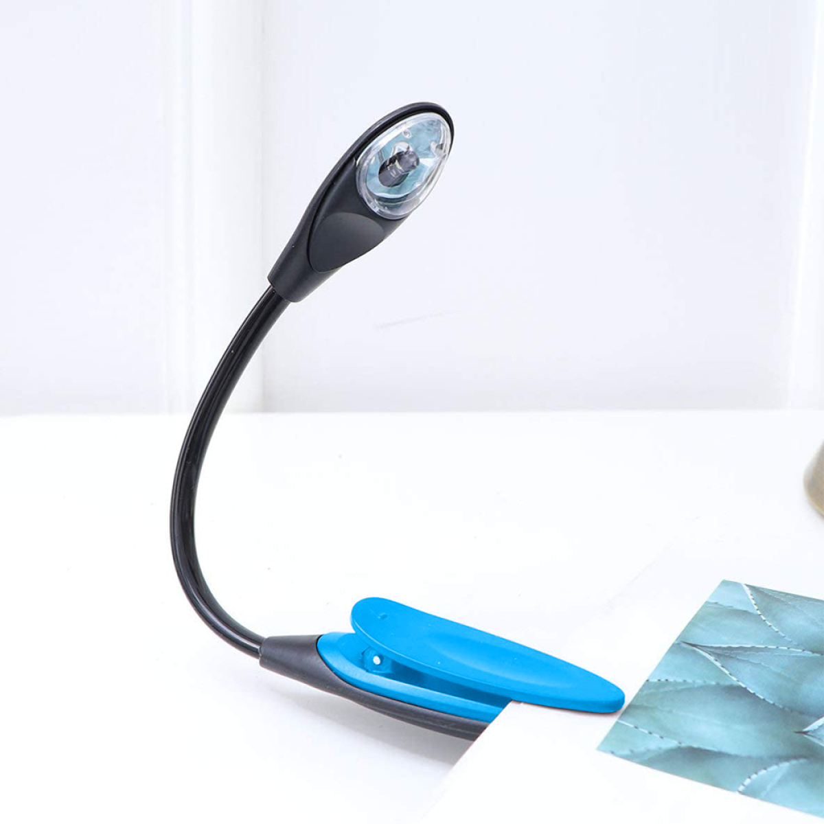 Eine schwarze und blaue Clip-on-Buchleuchte, an einer Seite befestigt. Das Licht ist an und beleuchtet die Seite.