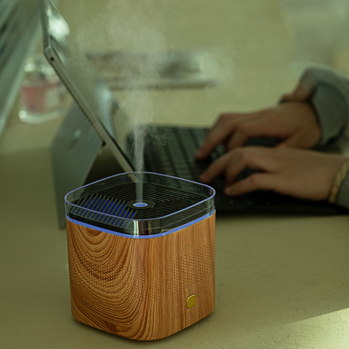 Ein Luftbefeuchter mit Holzsockel und blauem Deckel, mit aufsteigendem Dampf, auf einem Schreibtisch.