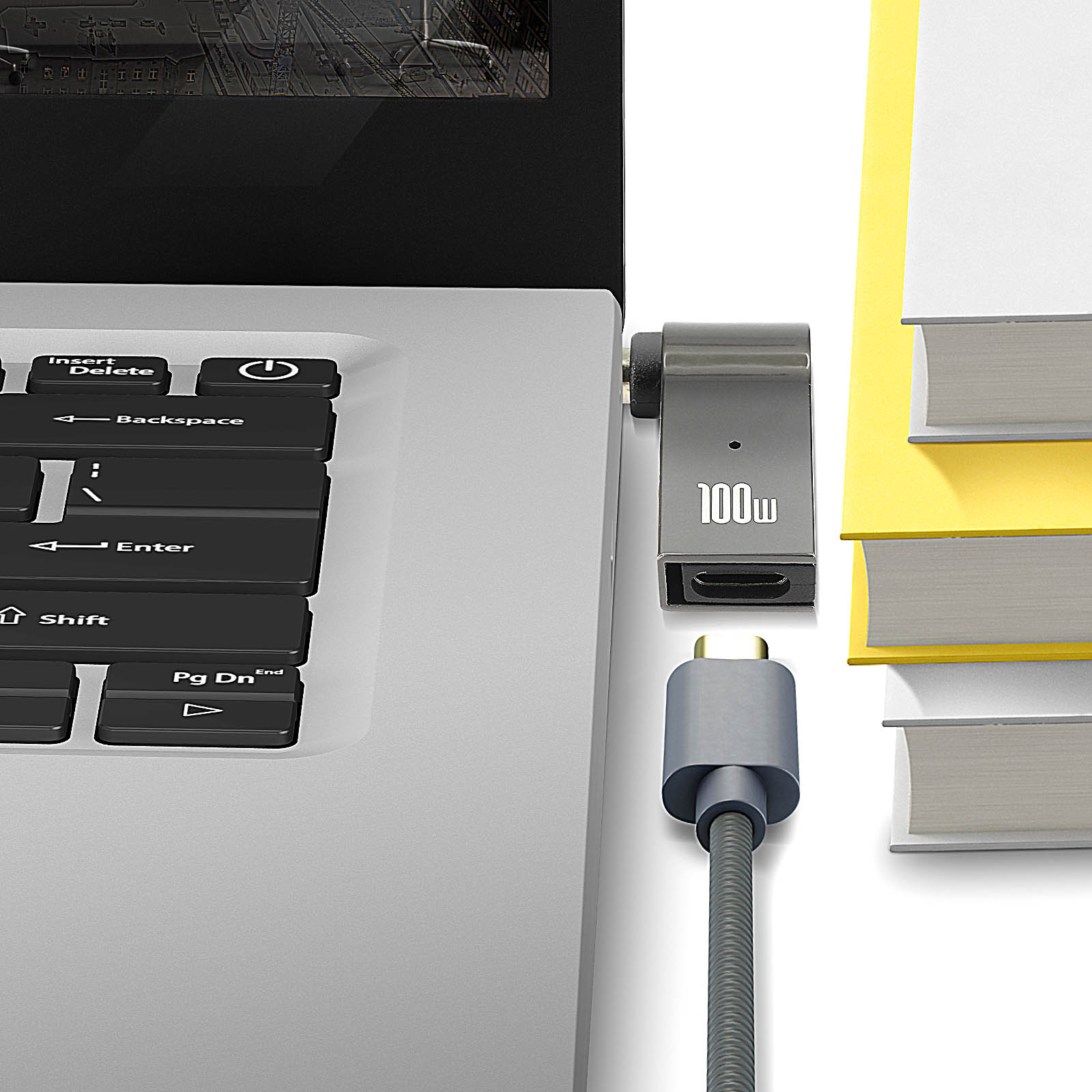 Un laptop con un cavo USB-C e un adattatore da 100w accanto a una pila di libri.