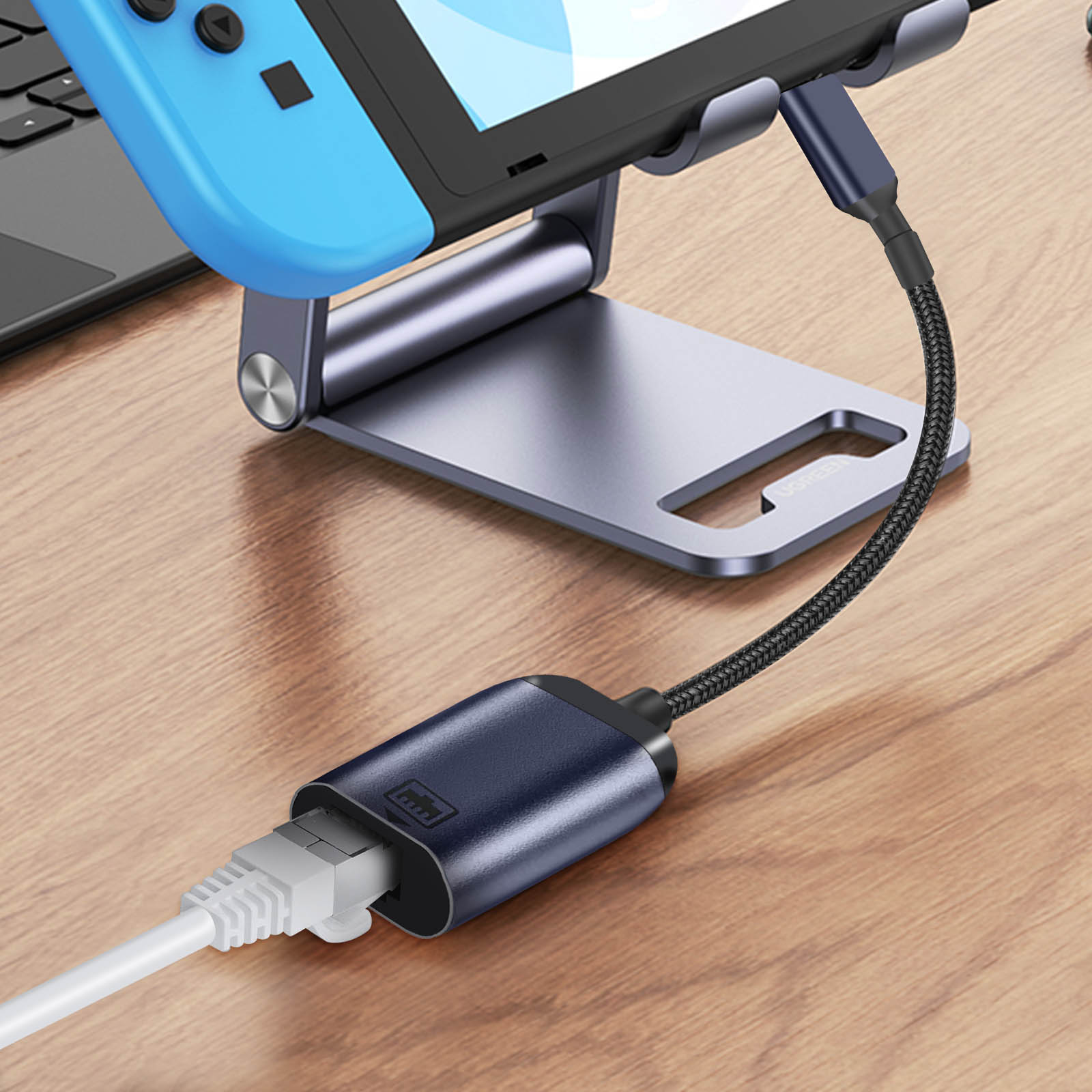 Un adattatore blu e nero collega un dispositivo di gioco a un cavo Ethernet, su una scrivania di legno.