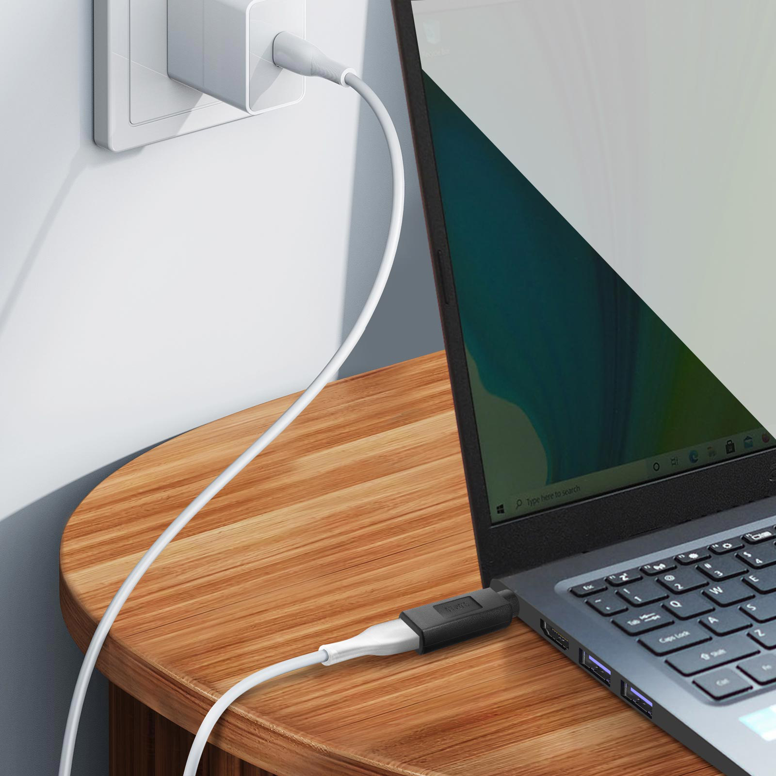 Laptop collegato a un caricabatterie su un tavolo di legno. Cavo bianco e adattatore nero visibili.