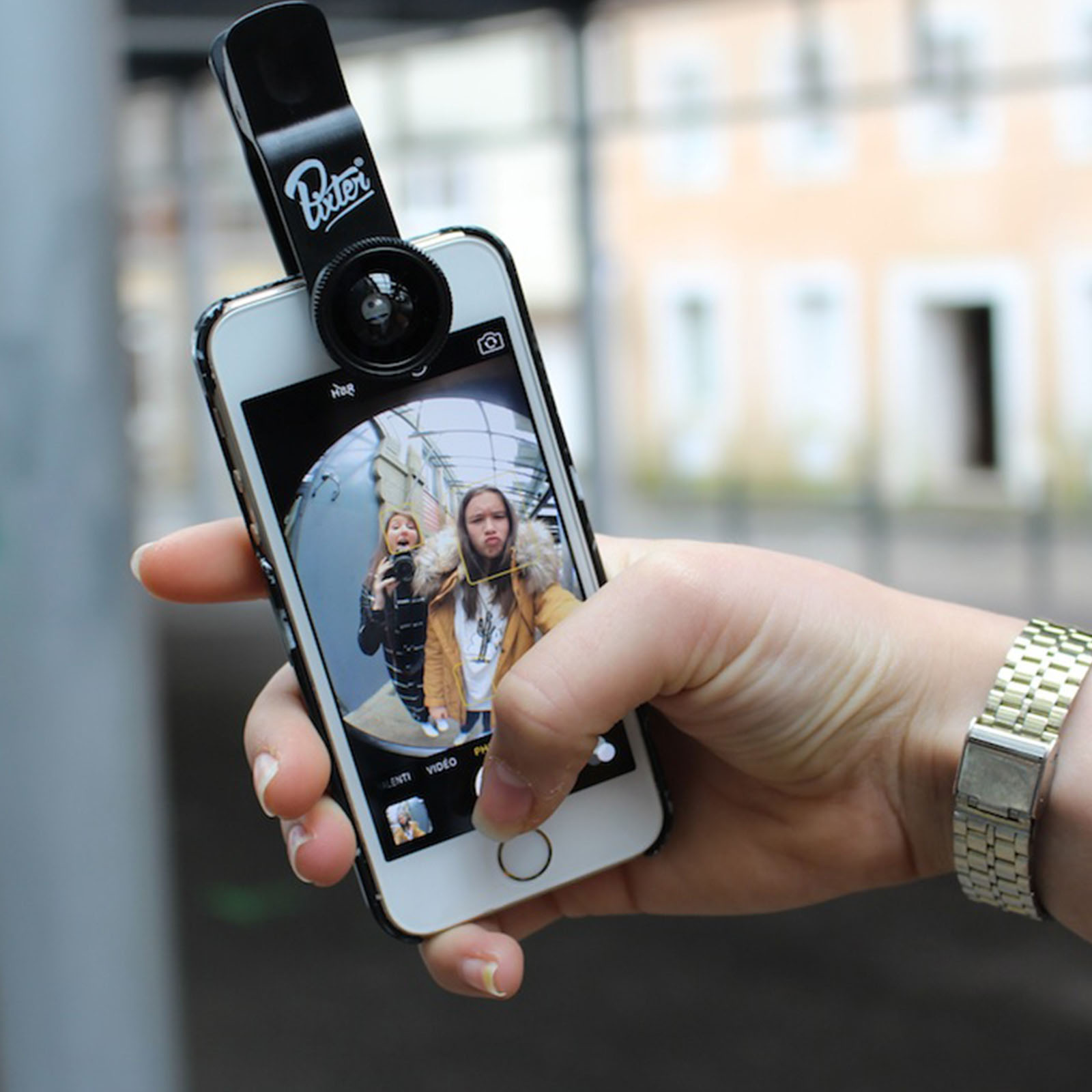Person hält Telefon mit Objektivaufsatz, macht Selfie mit zwei Personen.