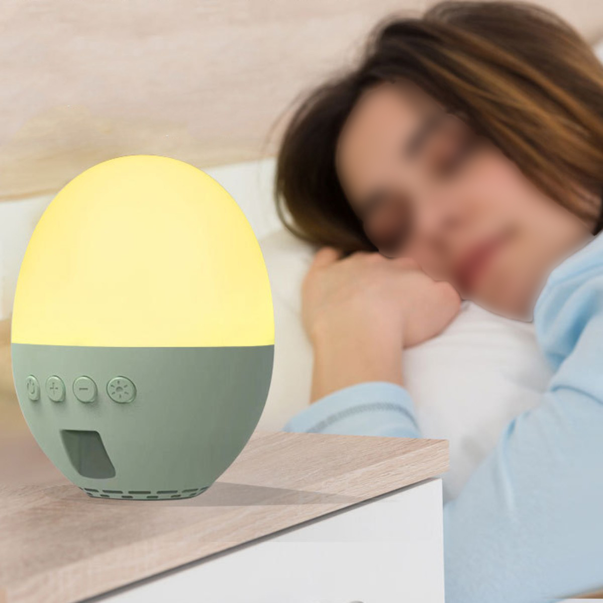 Eine Nachttischlampe mit rundem Oberteil und grünem Sockel neben einer schlafenden Person im Bett.