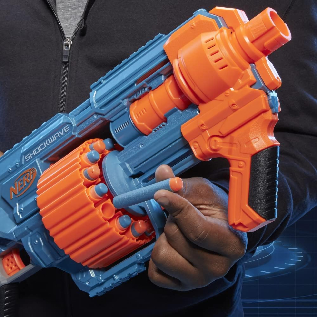 Osoba trzymająca niebiesko-pomarańczowy pistolet NERF SHOCKWAVE, z niebieską strzałką w dłoni.