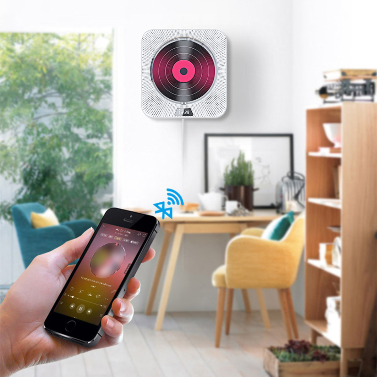 Eine Person hält ein Smartphone. Ein Wand-CD-Player spielt Musik. Tisch und Stühle im Hintergrund.