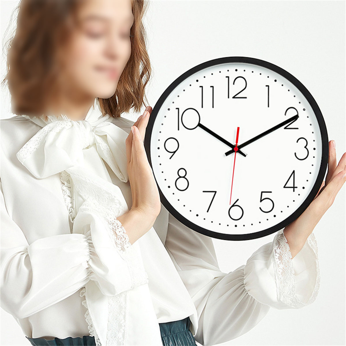 Una mujer sostiene un reloj blanco y negro. El reloj marca las 2:10. La mujer lleva una blusa blanca.