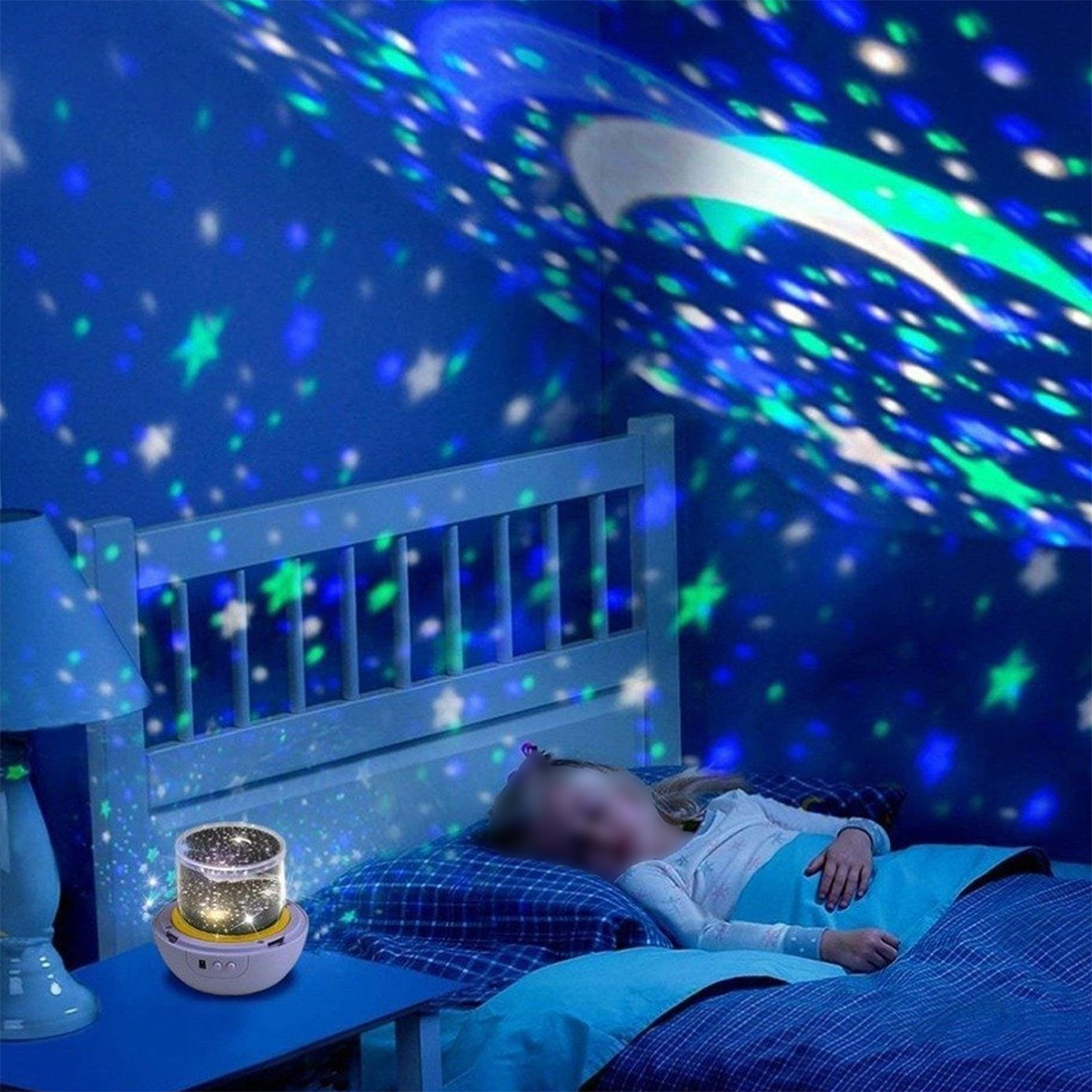 Un niño yace en la cama bajo una proyección de cielo estrellado. Un proyector en la mesita de noche emite la luz.