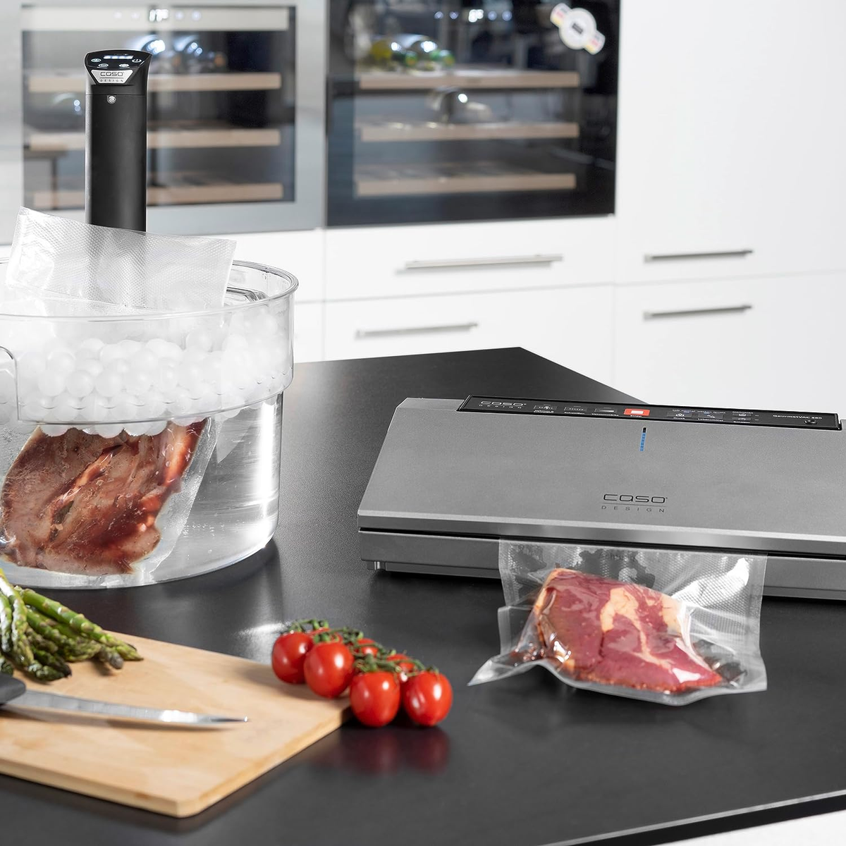 Sous-Vide-Setup mit vakuumversiegelten Lebensmitteln in Beuteln, neben einem Vakuumierer.
