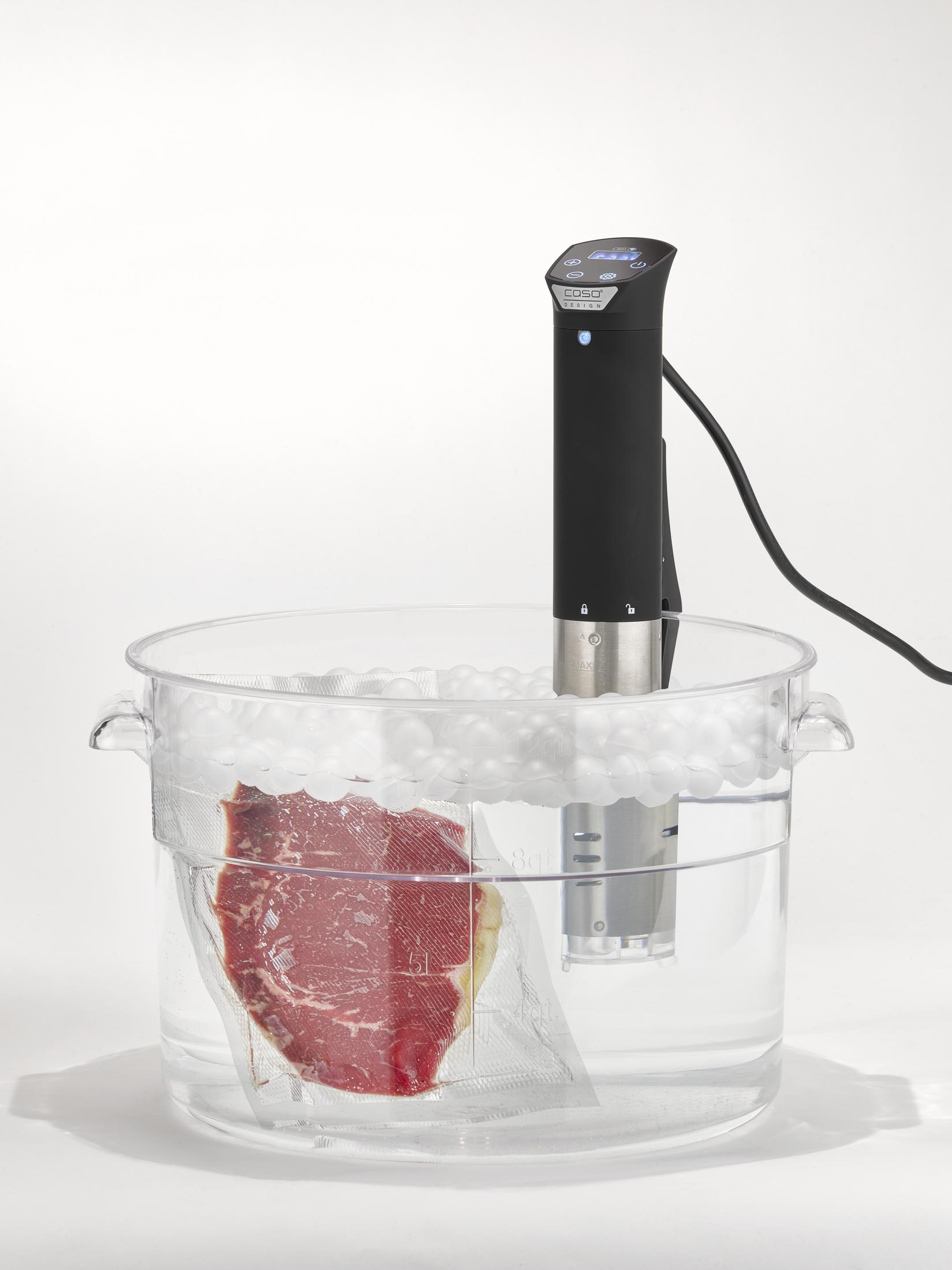 Sous-Vide-Gerät mit Steak im Beutel. Klarer Behälter und weißer Hintergrund.
