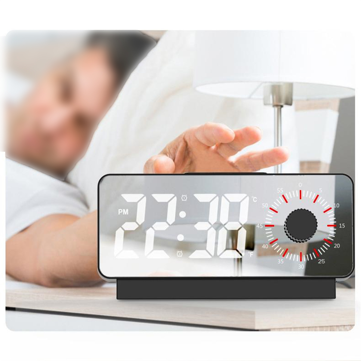 Ein digitaler Wecker mit Uhrzeit- und Temperaturanzeige, im Hintergrund eine verschwommene Person.