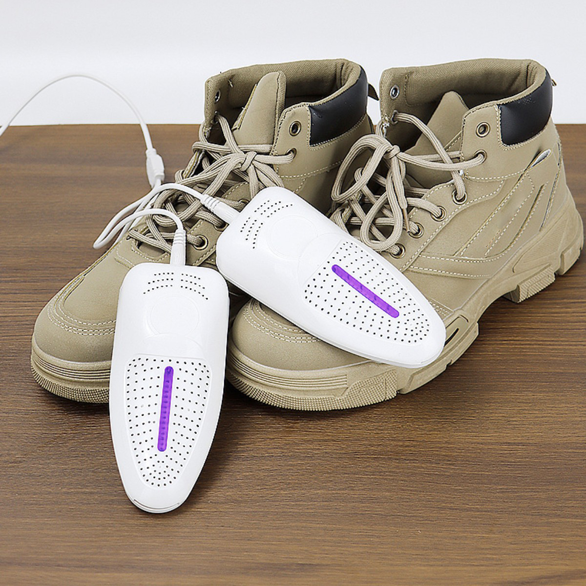 Zwei Schuhe werden von zwei weißen Schuhtrocknern auf einer Holzoberfläche getrocknet.