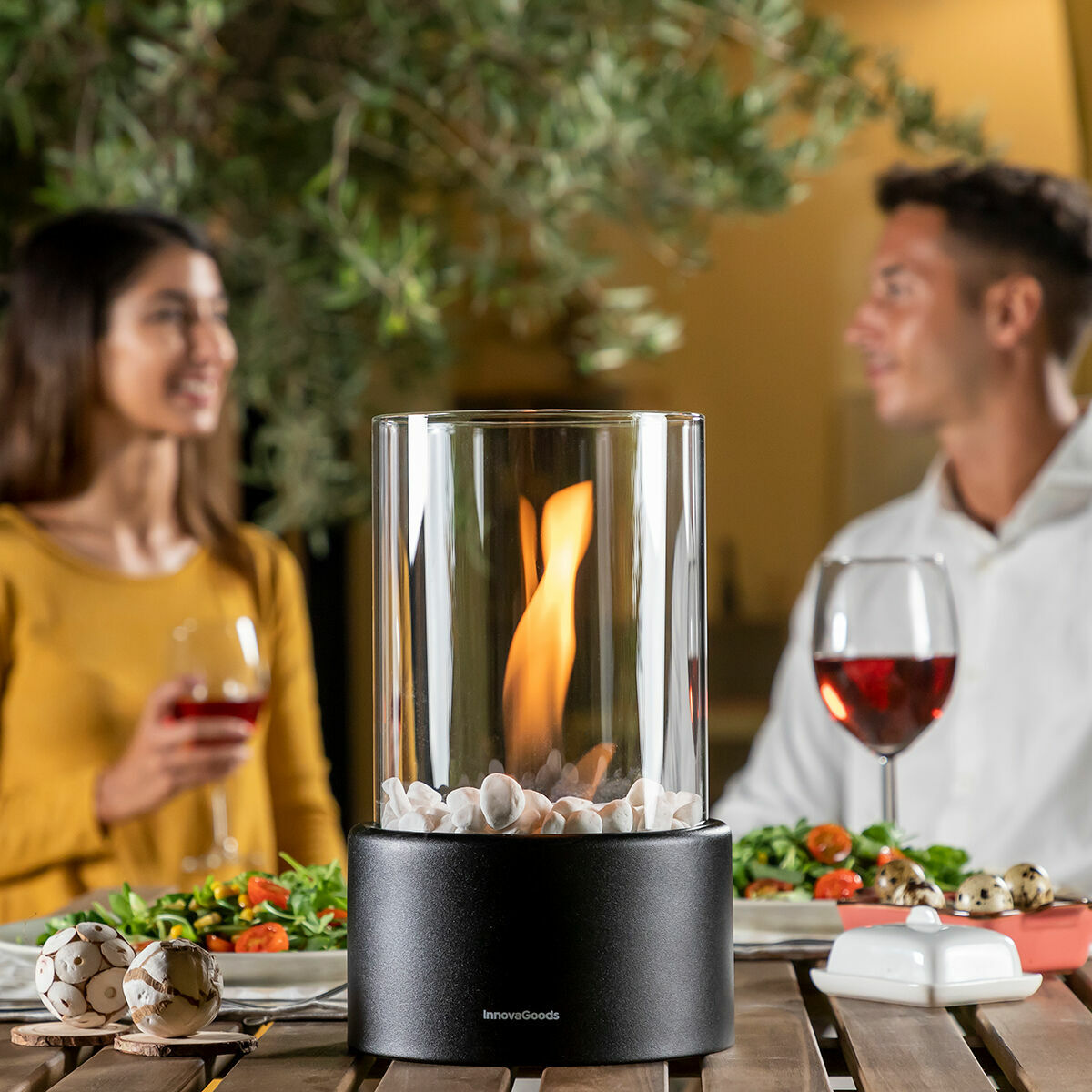 Paar sitzt an einem Tisch mit dekorativer Flamme, Weingläsern und Essen.