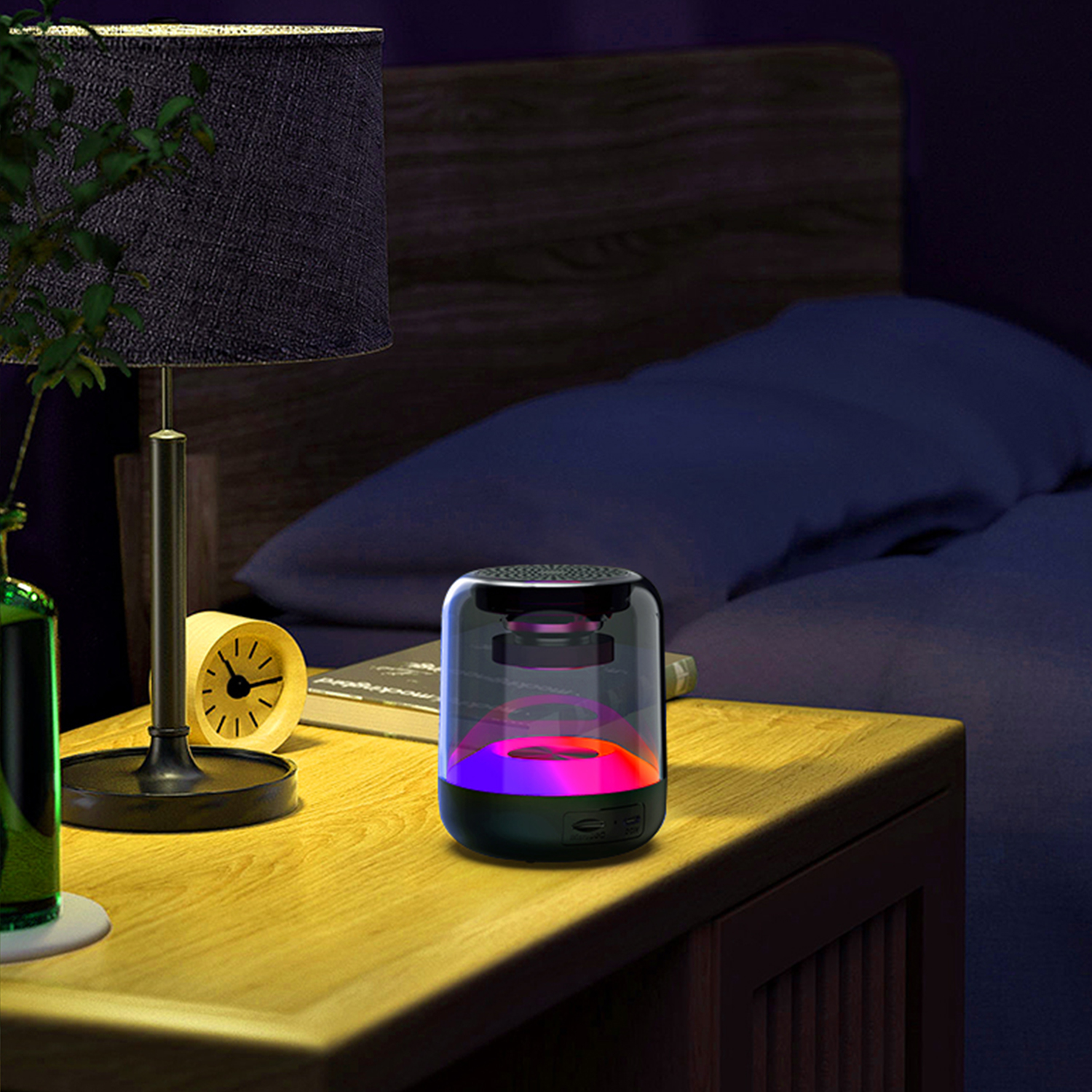 Altoparlante nero con luci che cambiano colore su un comodino, accanto a una lampada, un orologio e un libro.