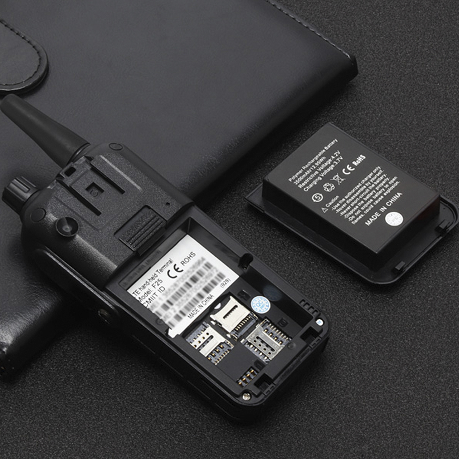 Walkie-talkie nero con vano batteria aperto e batteria staccata, su una superficie nera.
