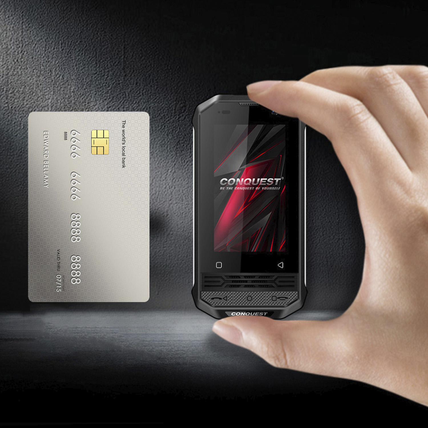 Una persona sosteniendo un pequeño smartphone negro resistente junto a una tarjeta de crédito.