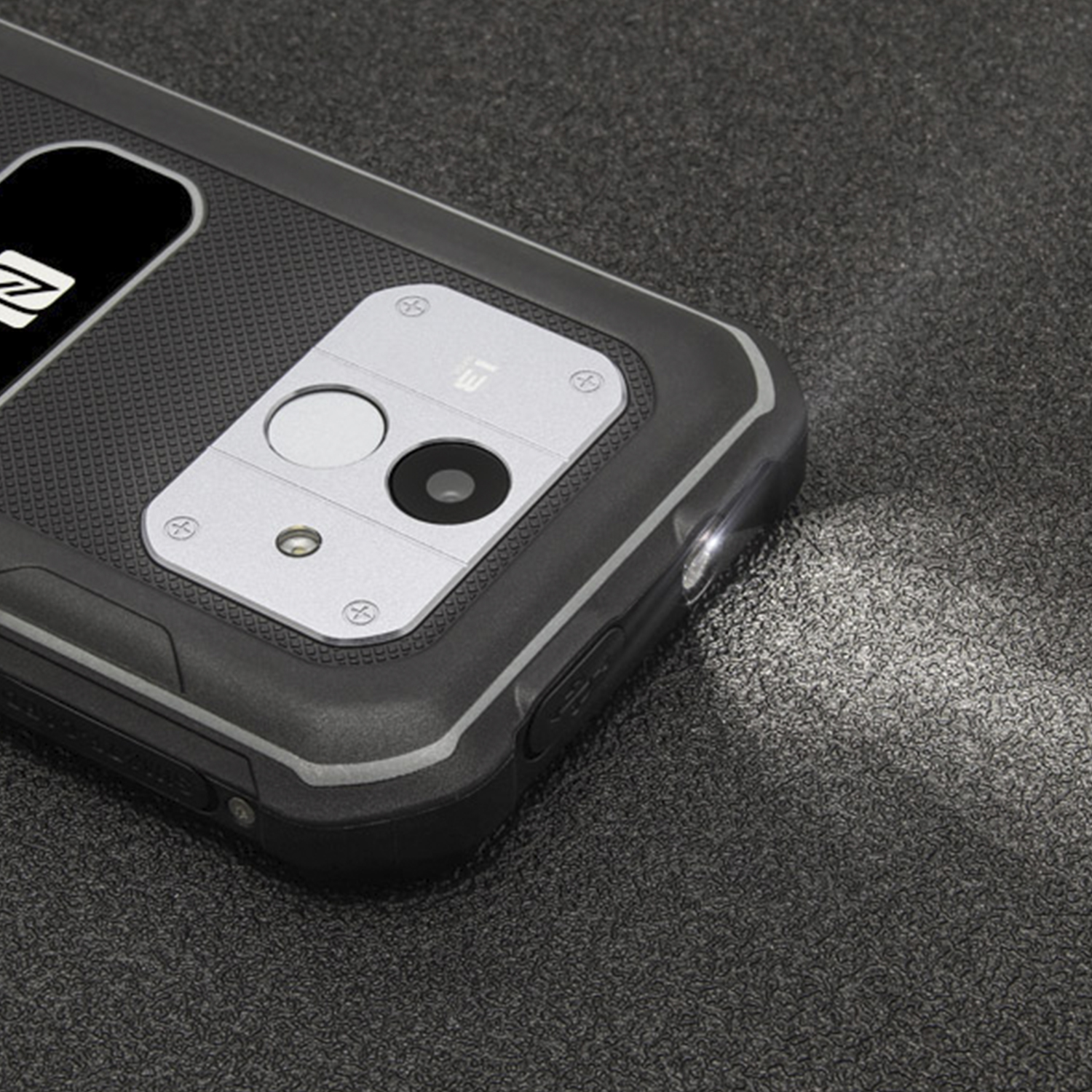 Un telefono nero robusto con torcia accesa. Una lente della fotocamera è visibile.