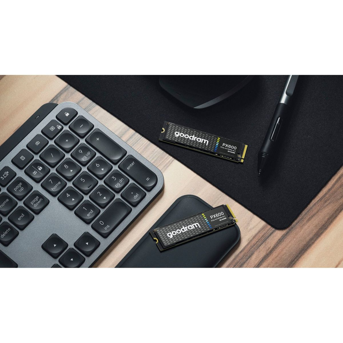 Klawiatura, podkładka pod mysz i dwa dyski SSD leżą na biurku. Dyski SSD są oznaczone jako „goodram PX600”.