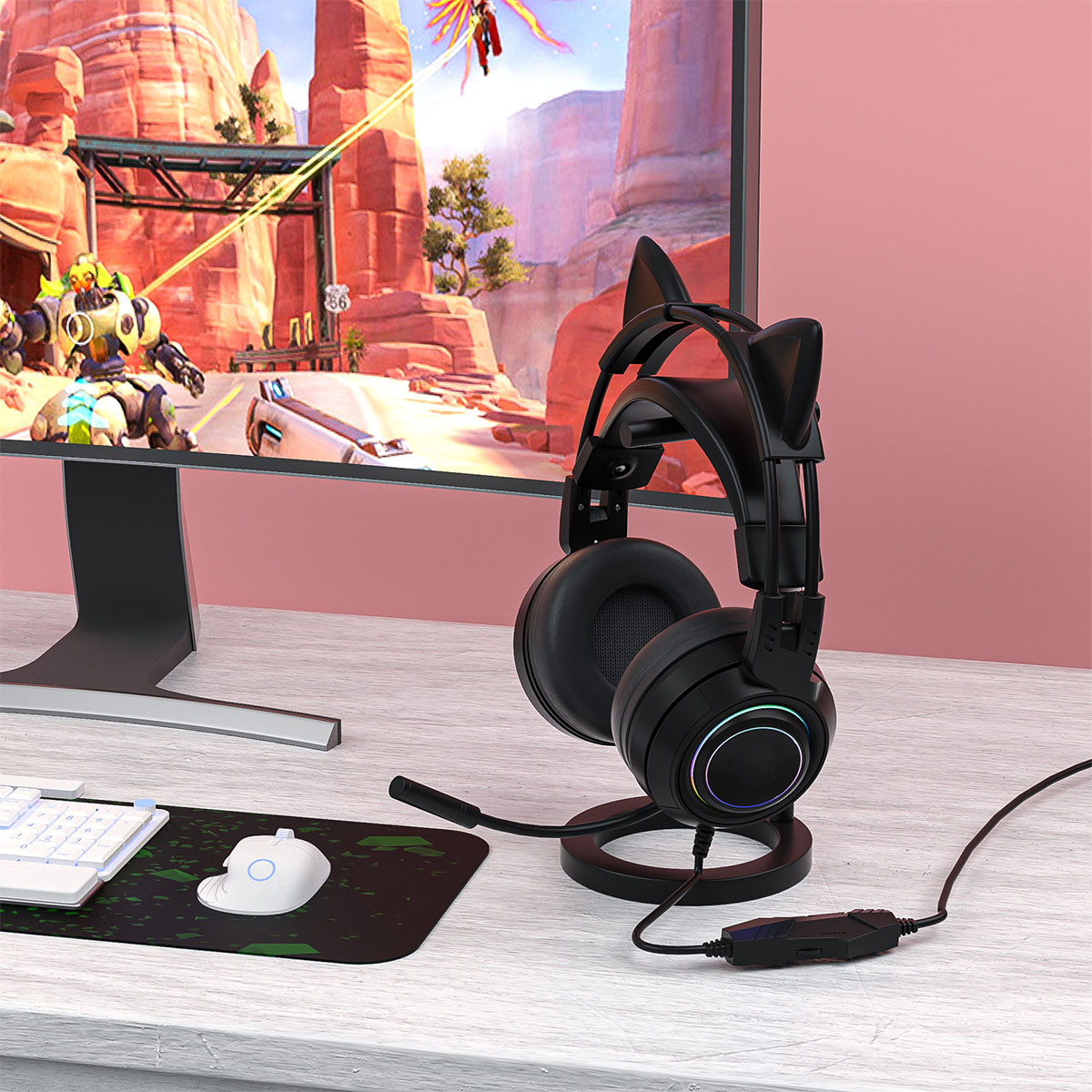 Schwarze Katzenohrhörer auf einem Ständer, ein Monitor mit einem Spiel, eine weiße Tastatur und eine Maus.