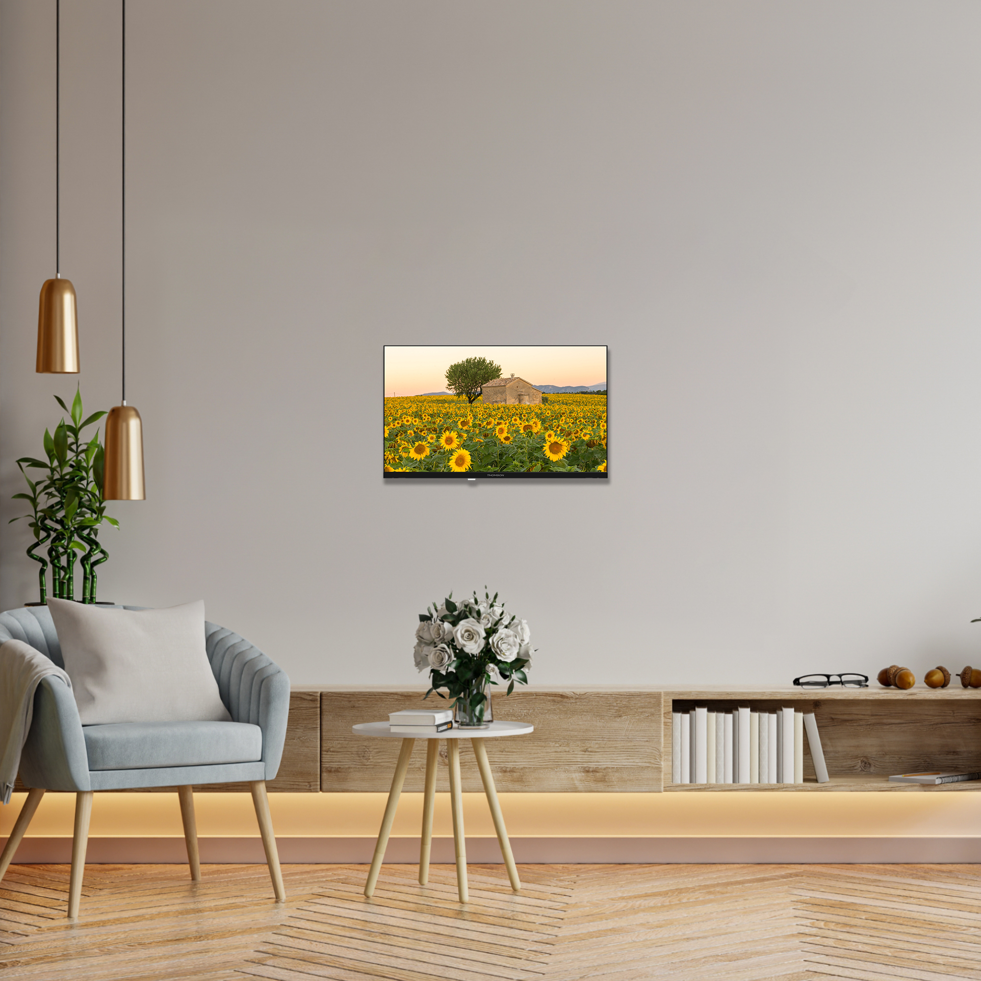 Una imagen enmarcada en una pared de un campo de girasoles y un pequeño edificio. Un sofá y una mesa con flores están en la escena.