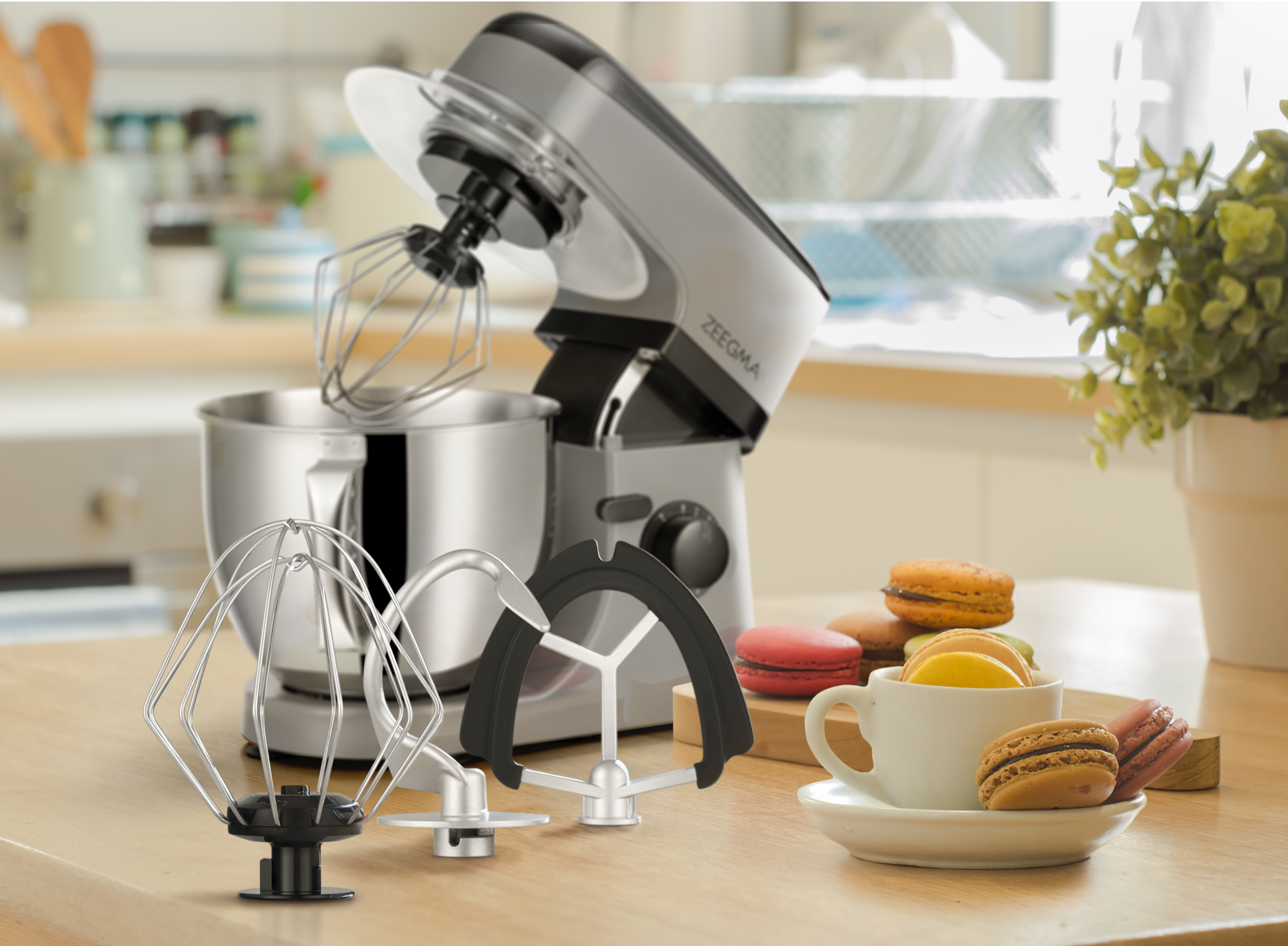 Srebrny mikser stojący z akcesoriami i makaronikami na drewnianym stole.