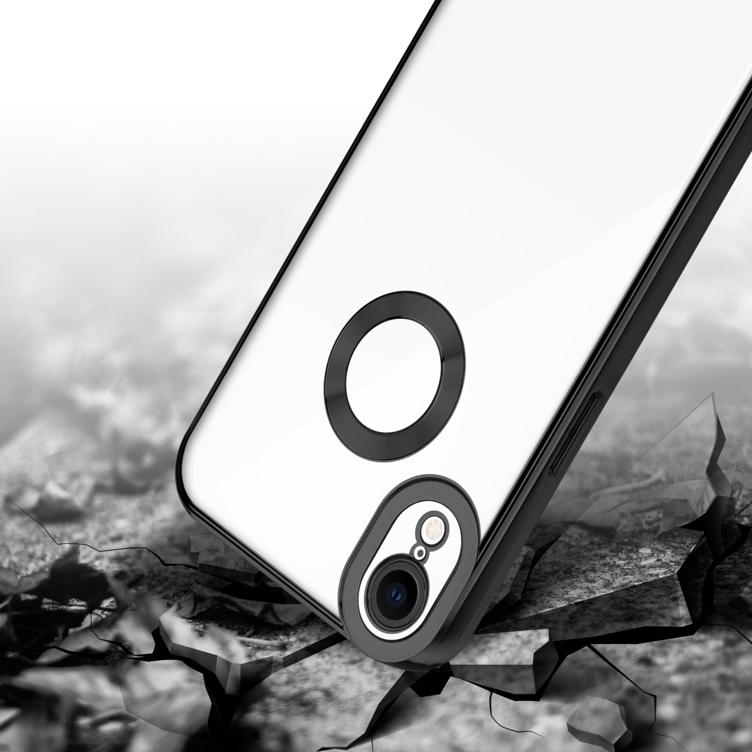 Telefono con custodia trasparente appoggiato su terreno crepato. Anello fotocamera nero, custodia bianca.