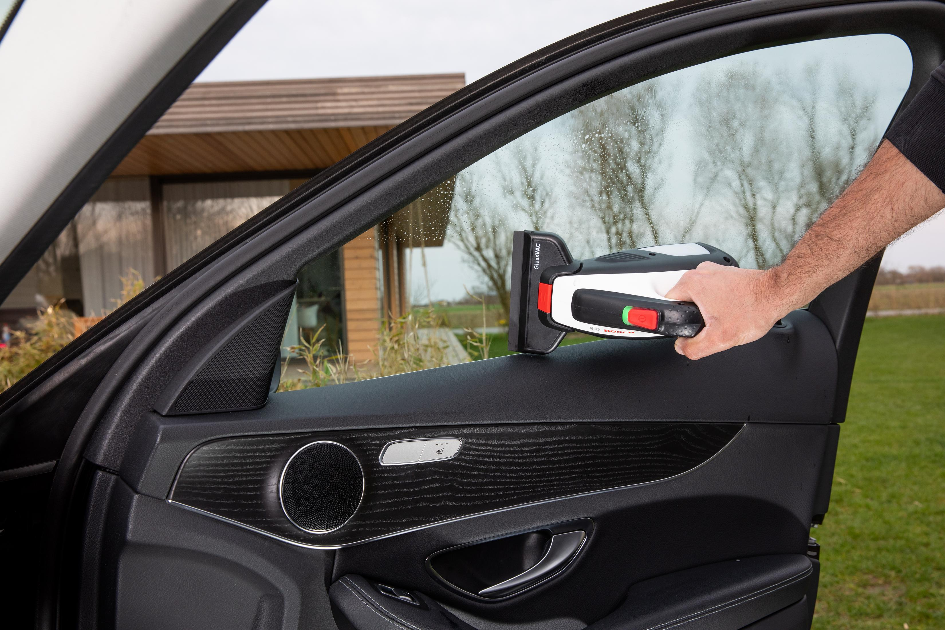 Osoba czyszcząca szybę w samochodzie urządzeniem ręcznym. Drzwi samochodu otwarte.