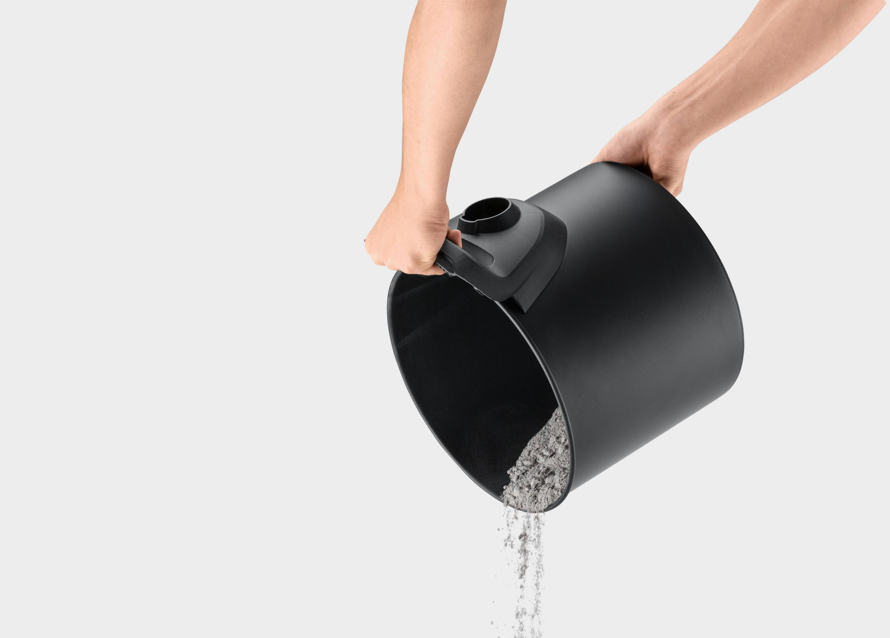 Czarny pojemnik odkurzacza jest trzymany do góry nogami. Popiół wylewa się na białe tło.