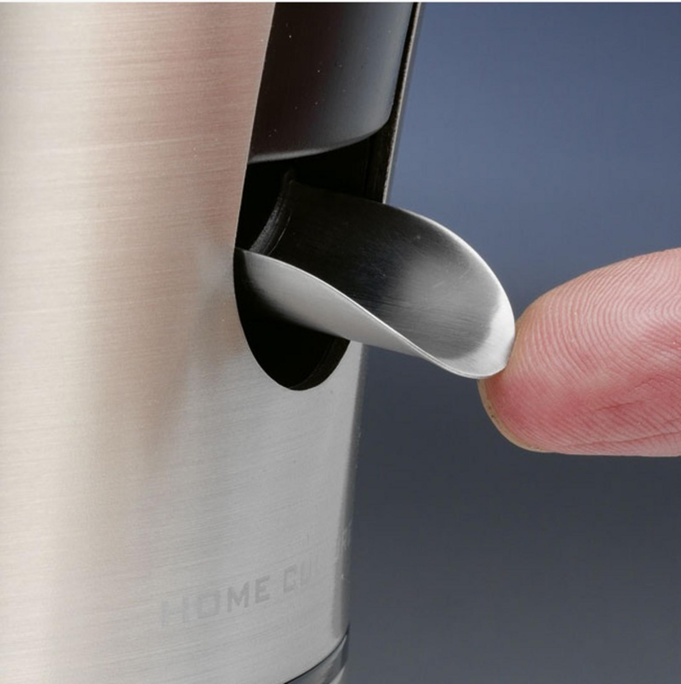 Ein Finger drückt einen Metallhebel an einem Metallbehälter. Der Hintergrund ist ein gedämpftes Grau.
