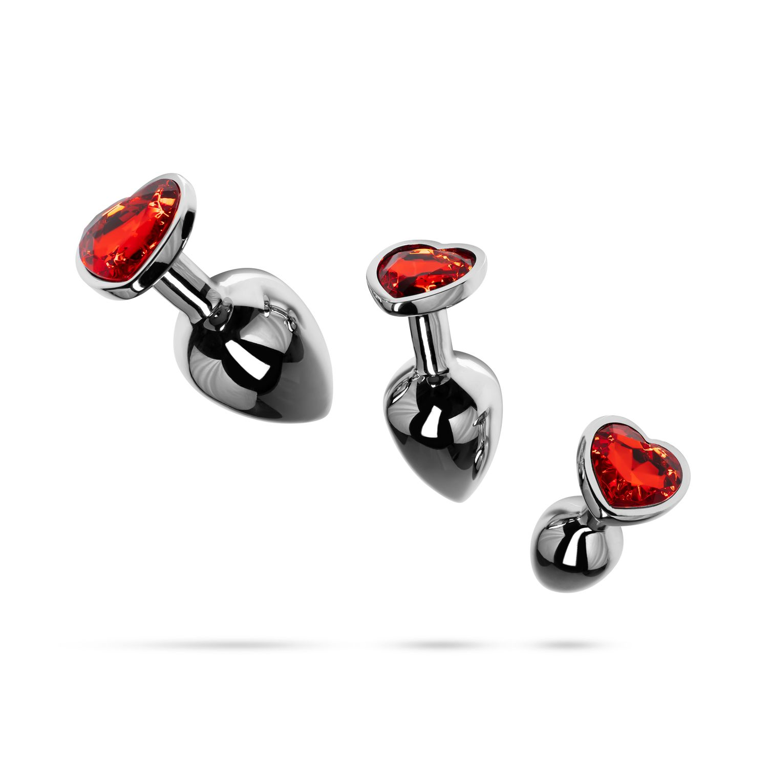 Drei Metall-Buttplugs mit herzförmigen roten Edelsteinen oben, diagonal angeordnet.