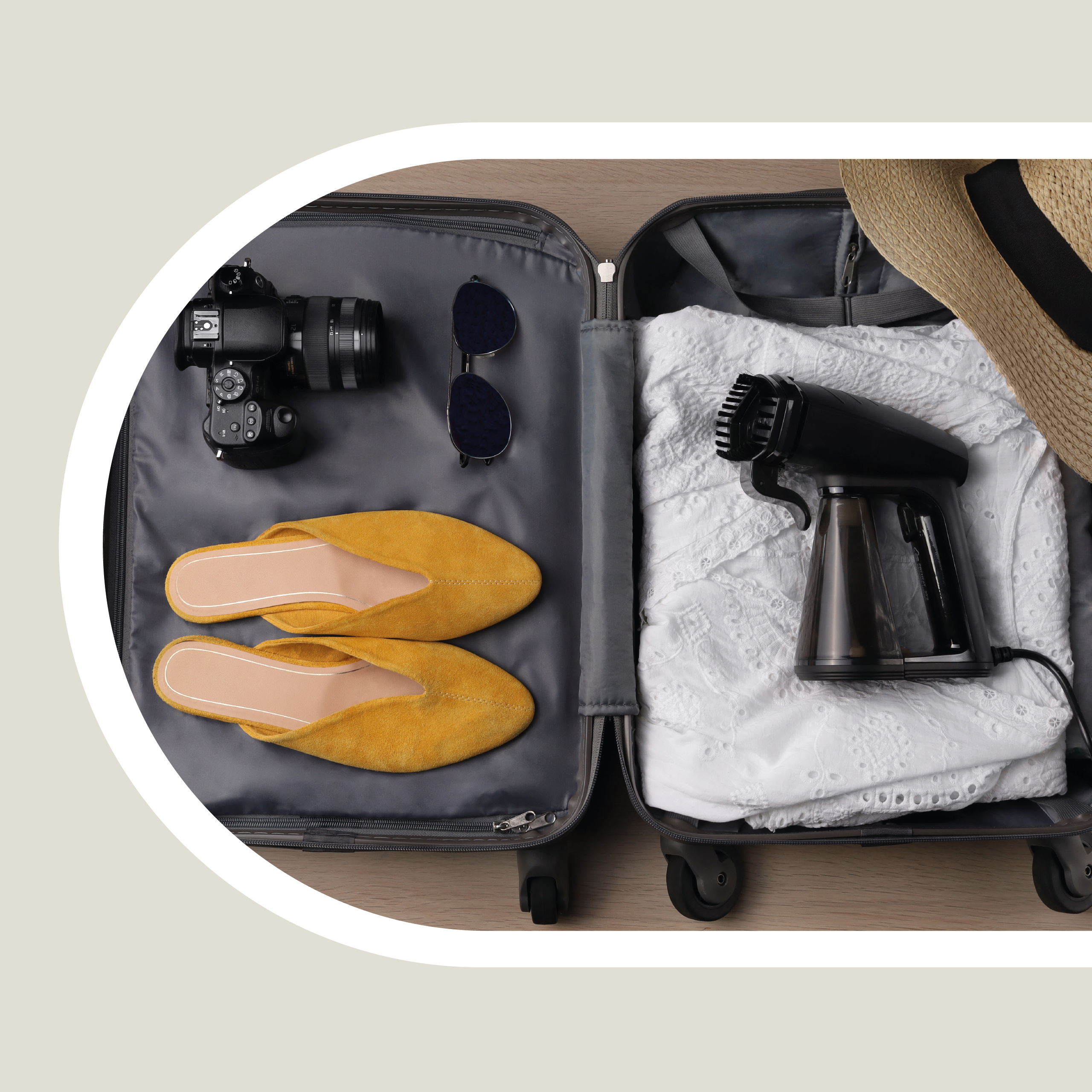 Otwarta walizka z ubraniami, butami, aparatem, okularami przeciwsłonecznymi i parownicą w środku.