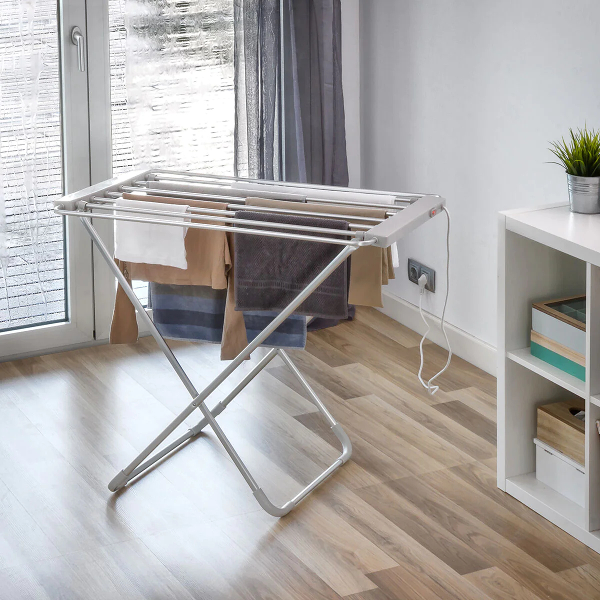 Un tendedero eléctrico blanco se encuentra en el interior con ropa y un cable de alimentación visibles.
