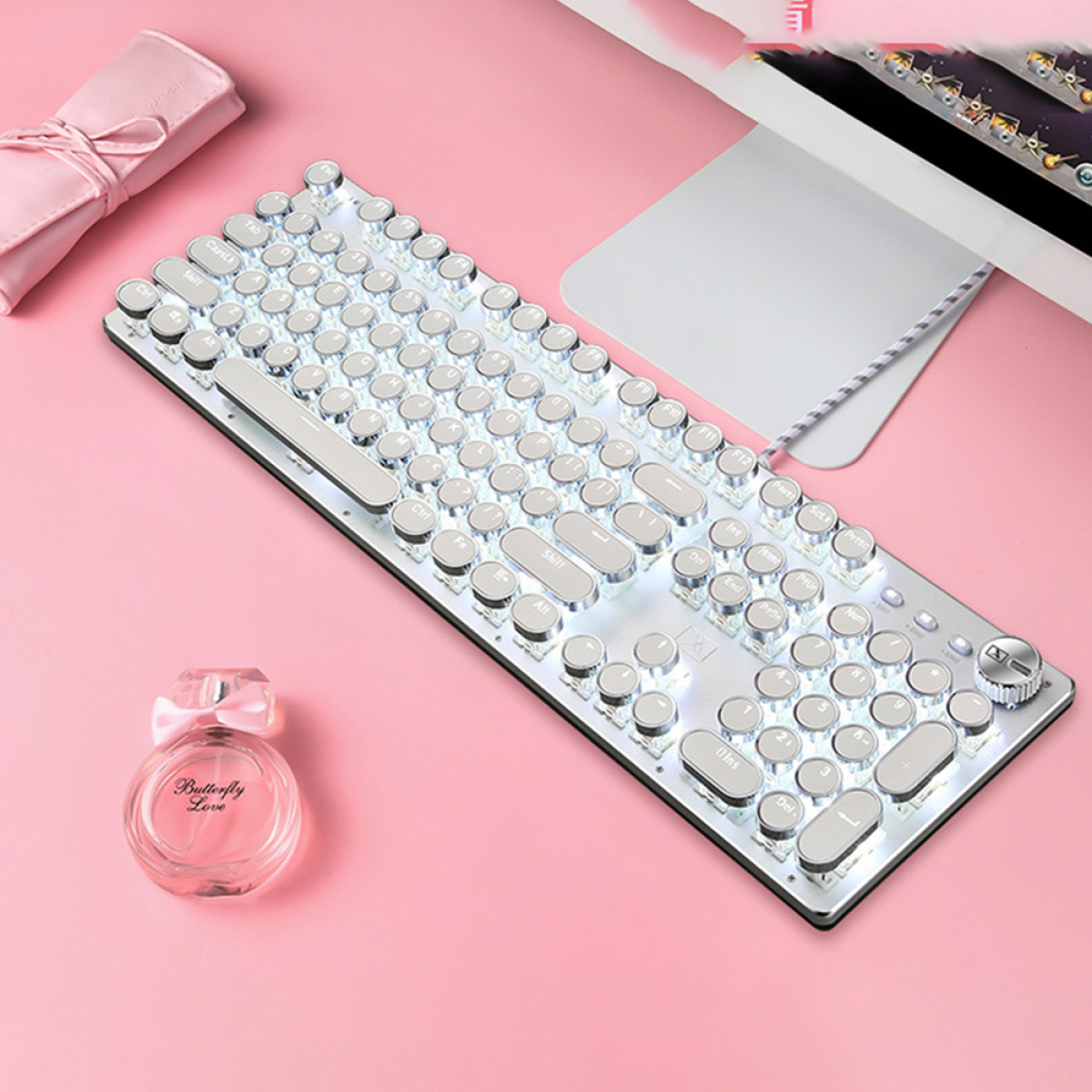 Eine silberne Retro-Tastatur mit weißen Tasten und eine Parfümflasche auf rosa Oberfläche.
