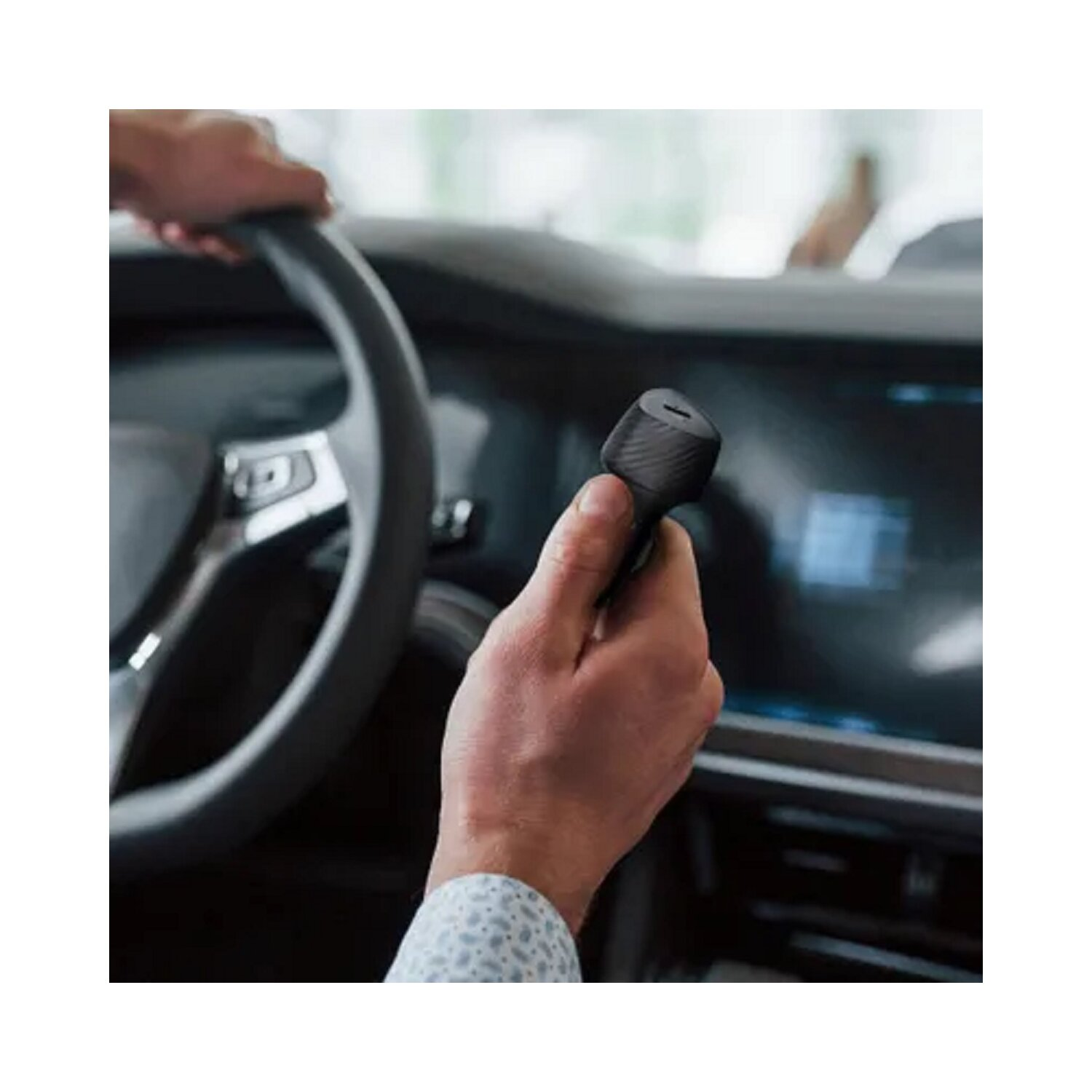 Eine Person hält ein schwarzes Autoladegerät in einem Auto. Das Ladegerät ist zylindrisch und hat einen strukturierten Griff.