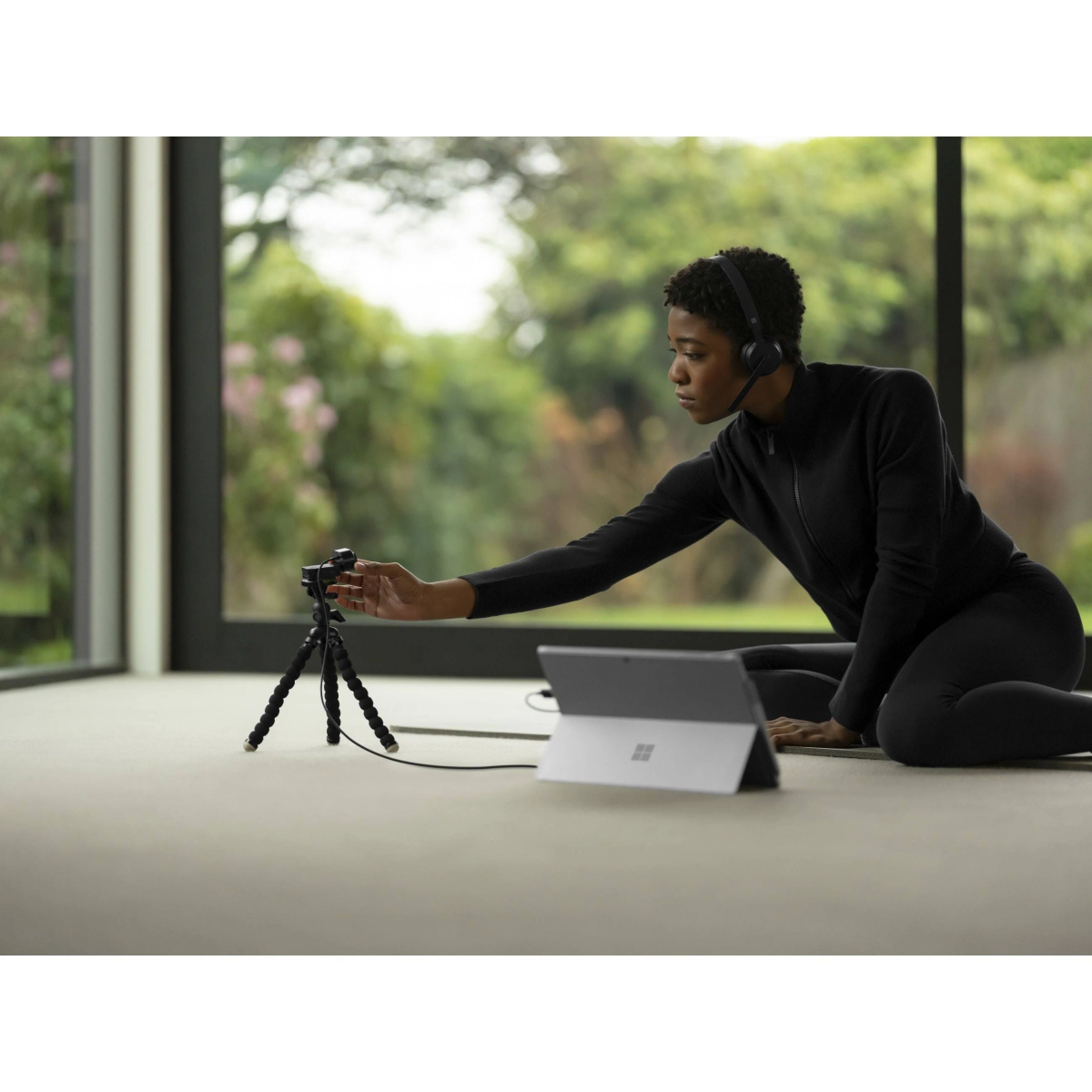 Kobieta w czarnym stroju używa tabletu i statywu do wideo, widoczny ogród.