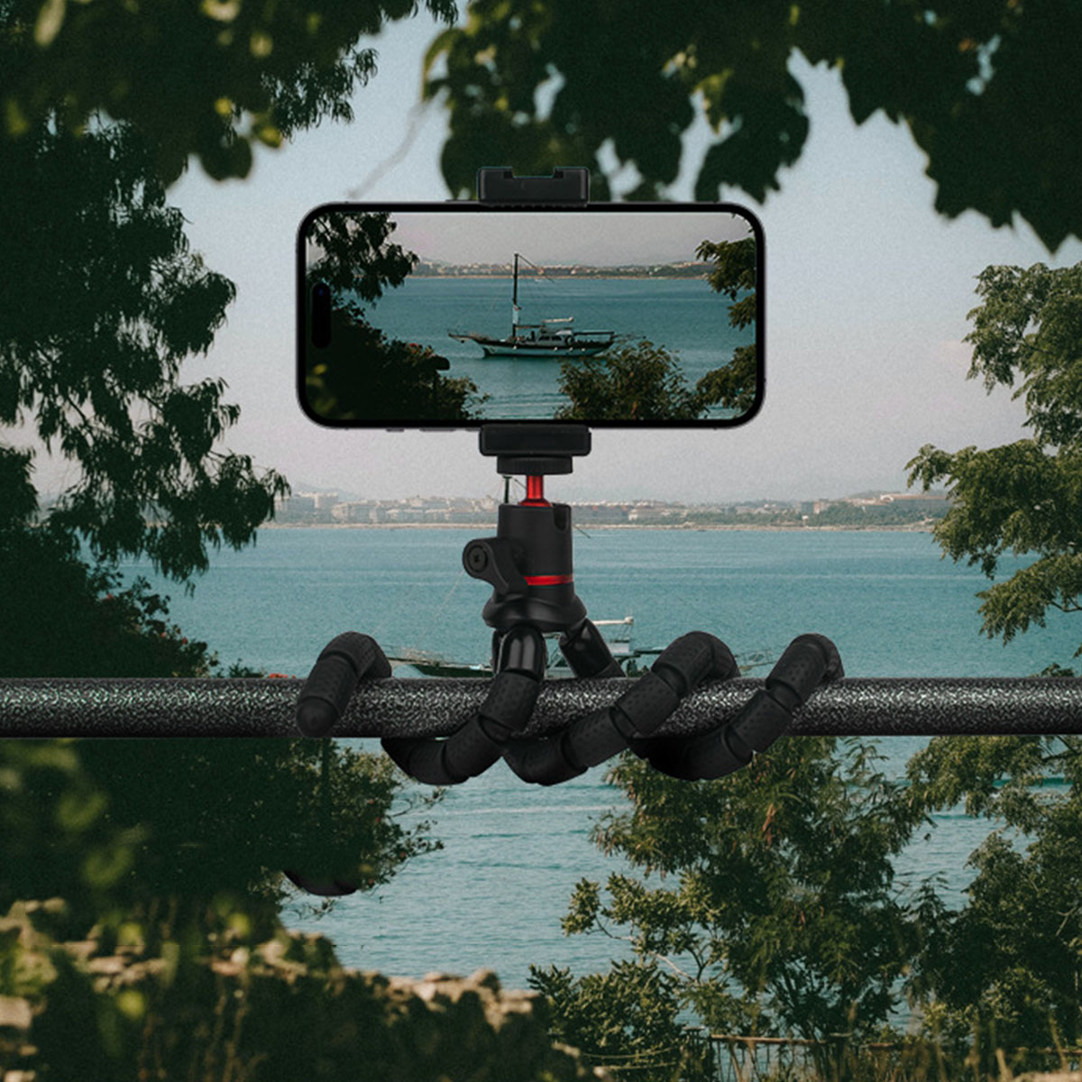 Ein Telefon auf einem flexiblen Stativ, das ein Boot auf dem Meer filmt. Die Szene wird von Bäumen umrahmt.