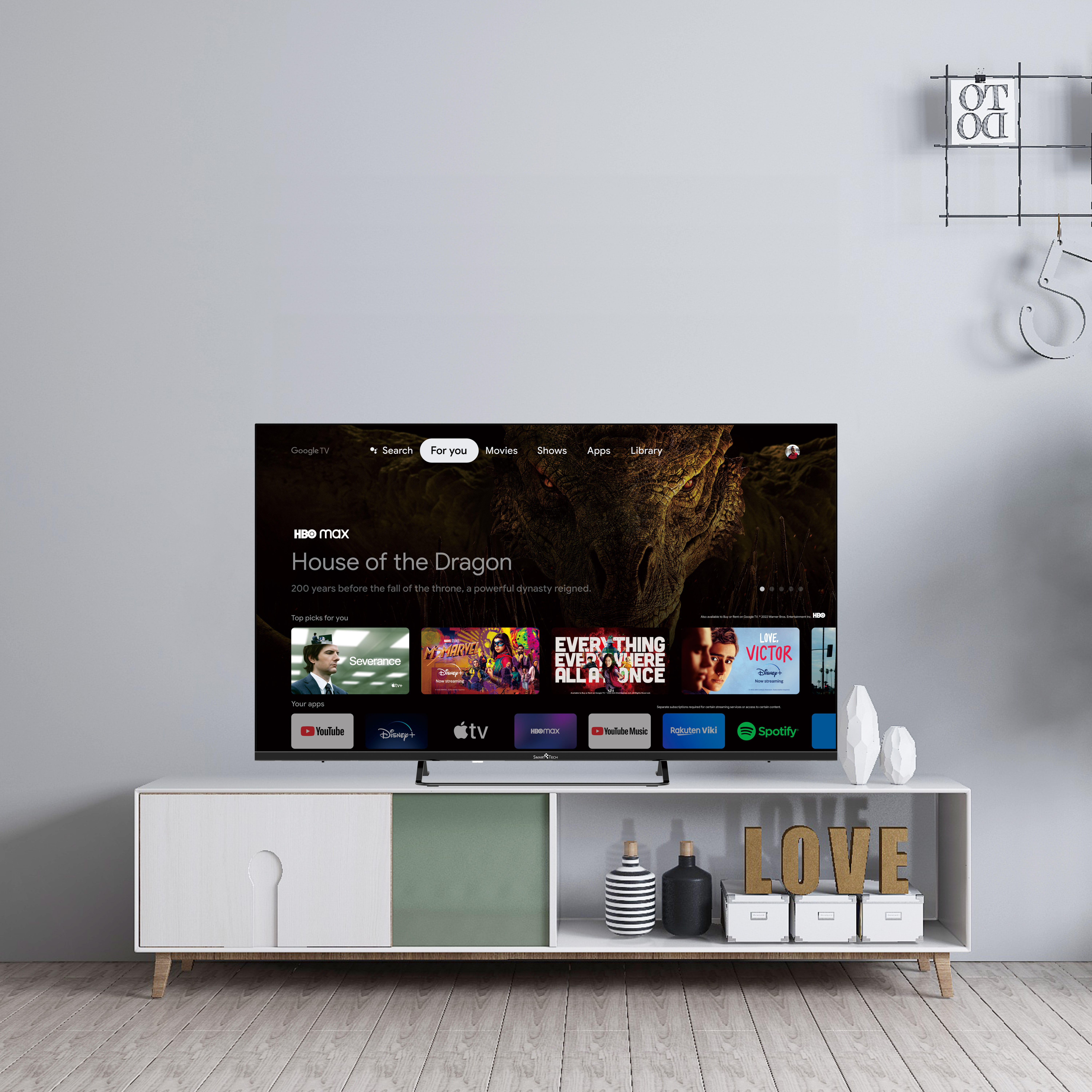 Pantalla de TV que muestra la película "House of the Dragon". Un mueble de entretenimiento blanco y decoraciones debajo.