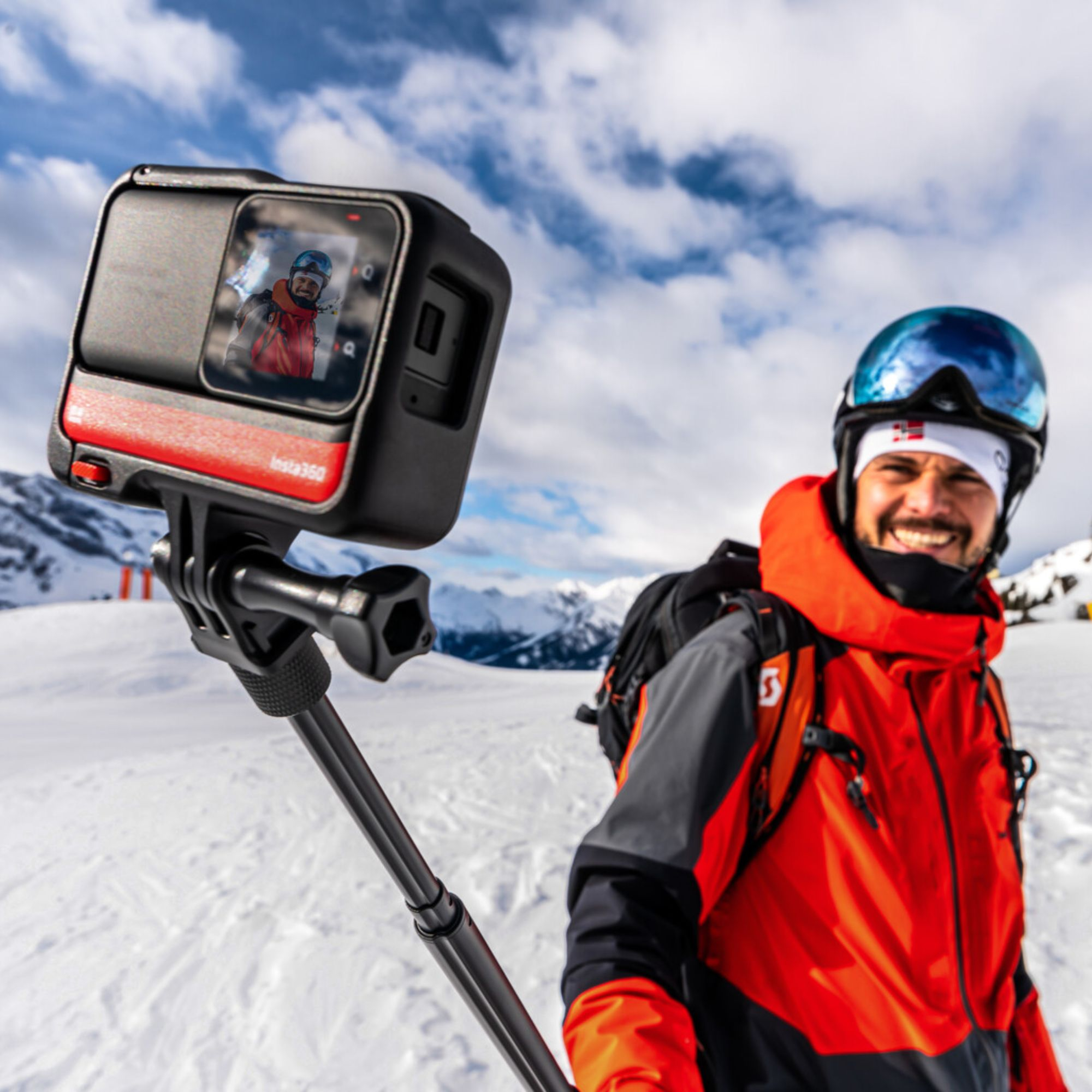 Ein Mann hält eine schwarze Action-Kamera auf einem Selfie-Stick im Schnee. Er lächelt.