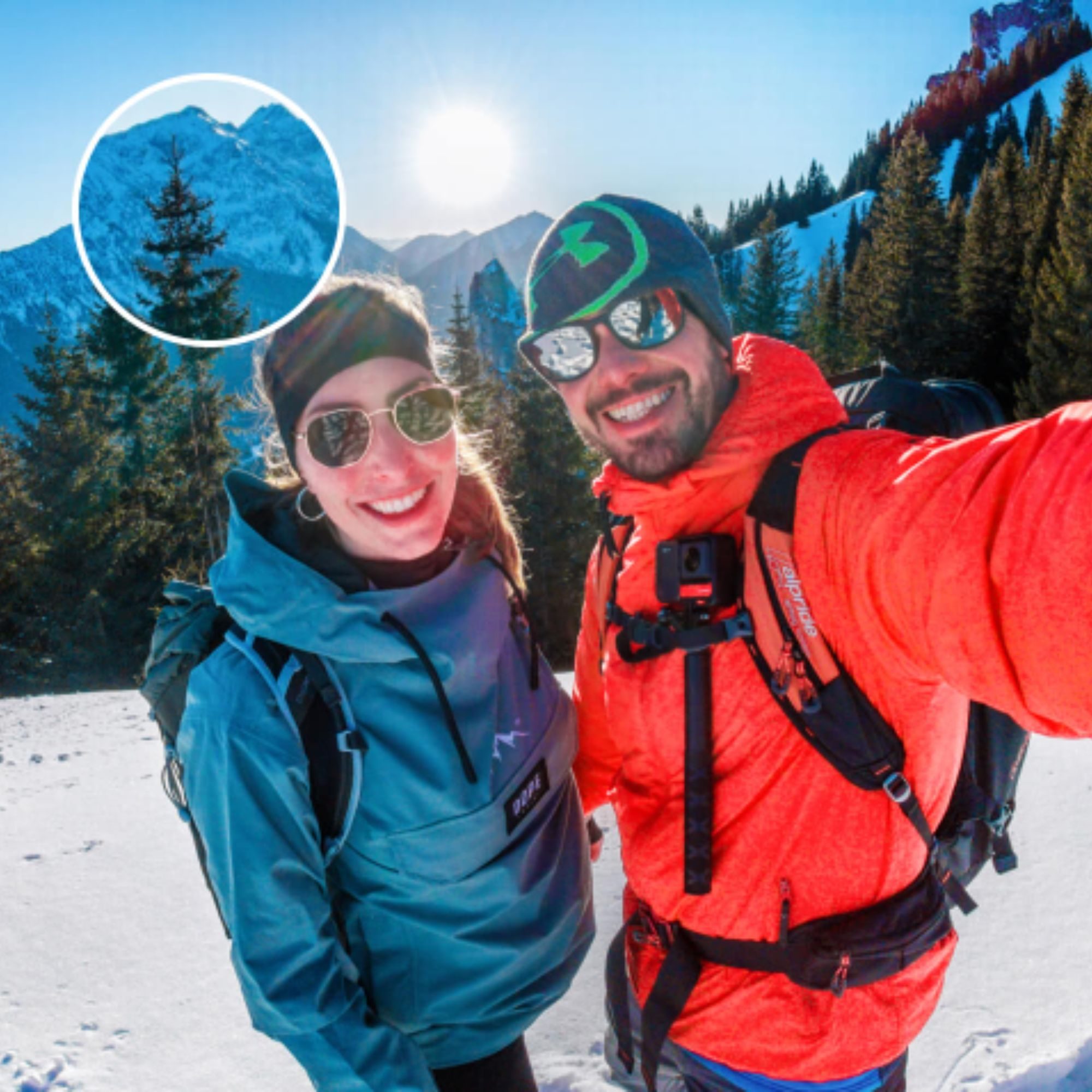 Zwei lächelnde Personen, die Sonnenbrillen tragen, in einer schneebedeckten Berglandschaft.