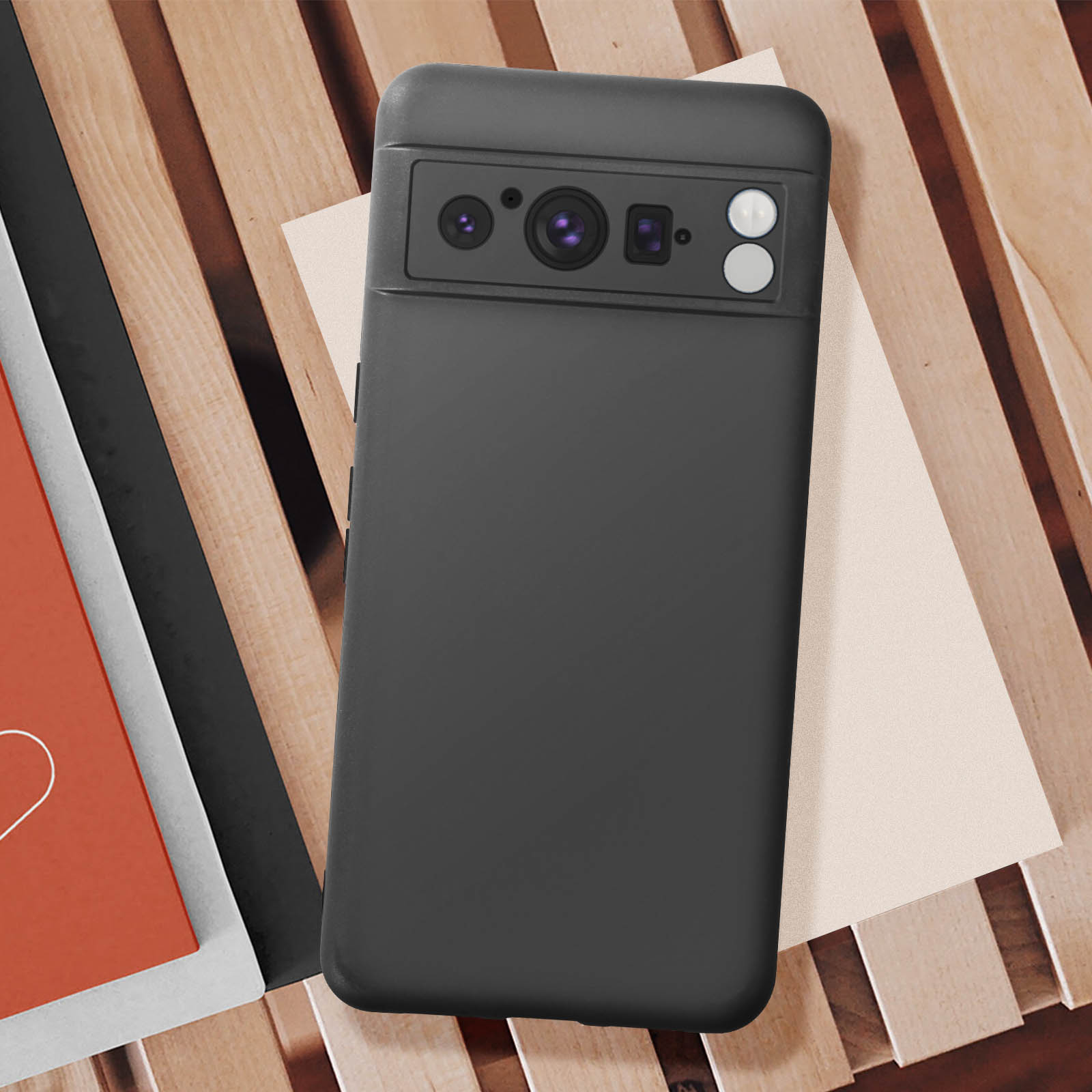 Custodia nera per telefono su una superficie di legno con libri. Presenta un ritaglio per la fotocamera e il logo Google.