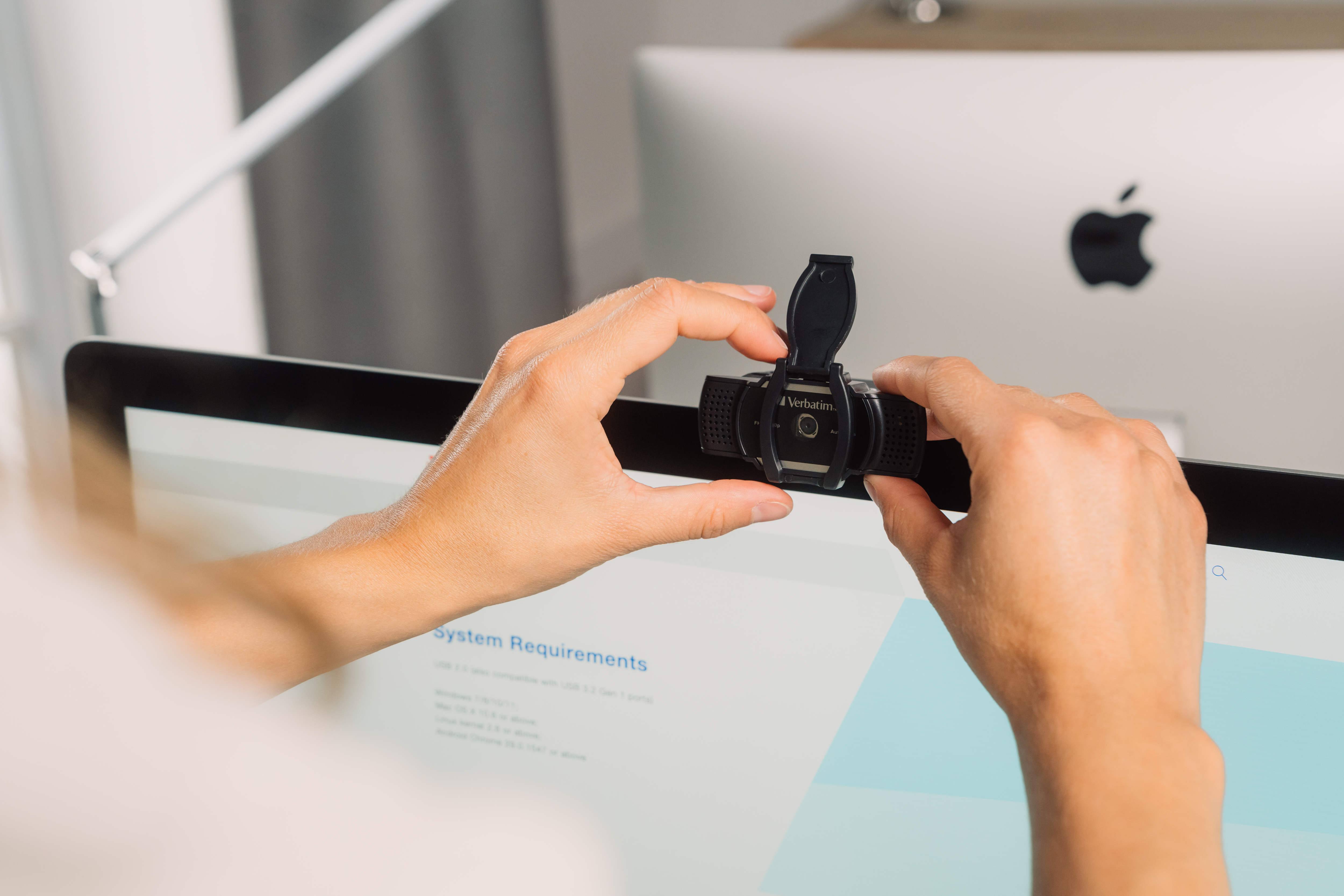 Osoba mocująca czarną kamerę internetową do monitora komputera.
